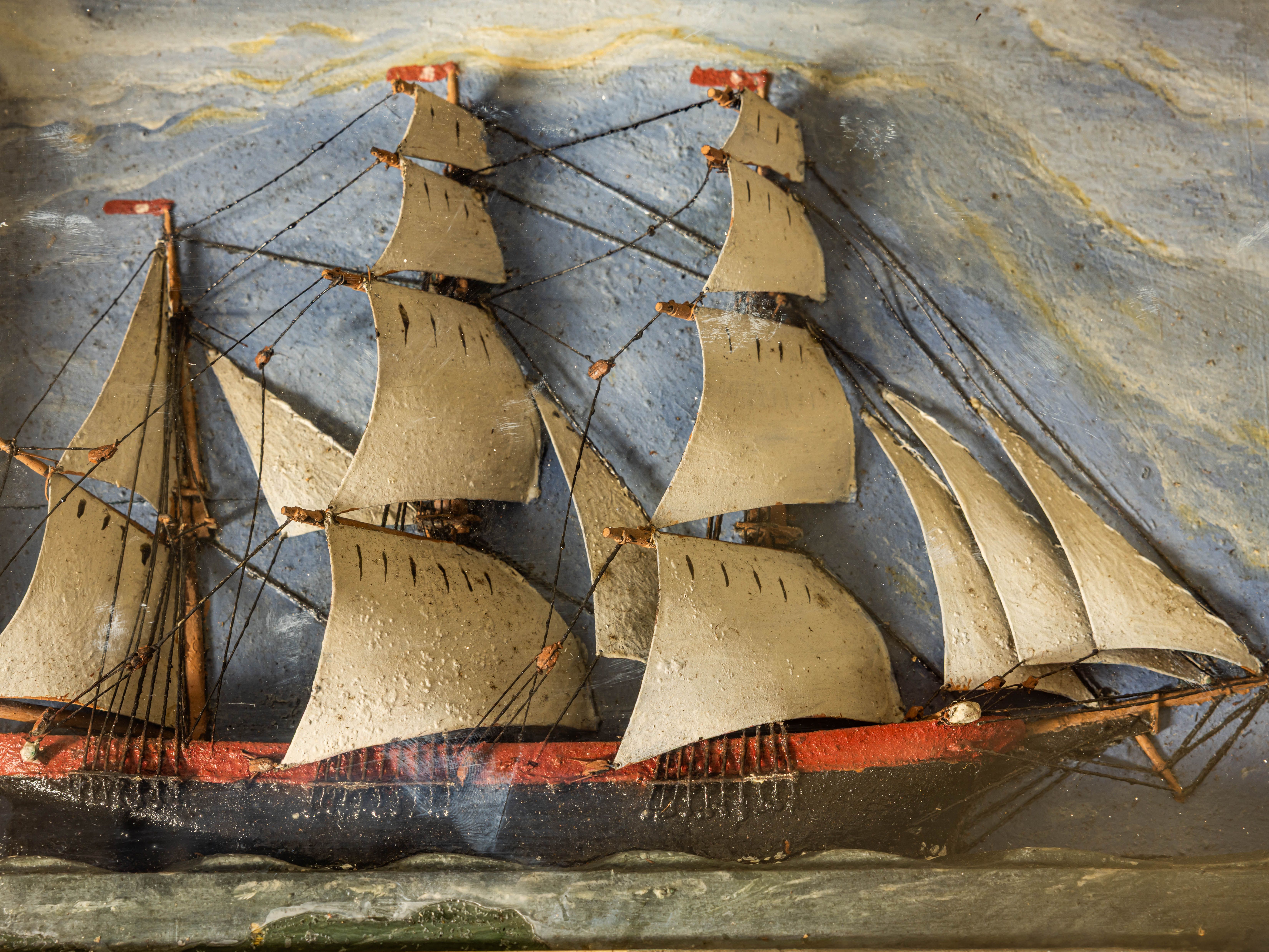 Model of a sailing ship with multiple sails against a painted sea and sky backdrop