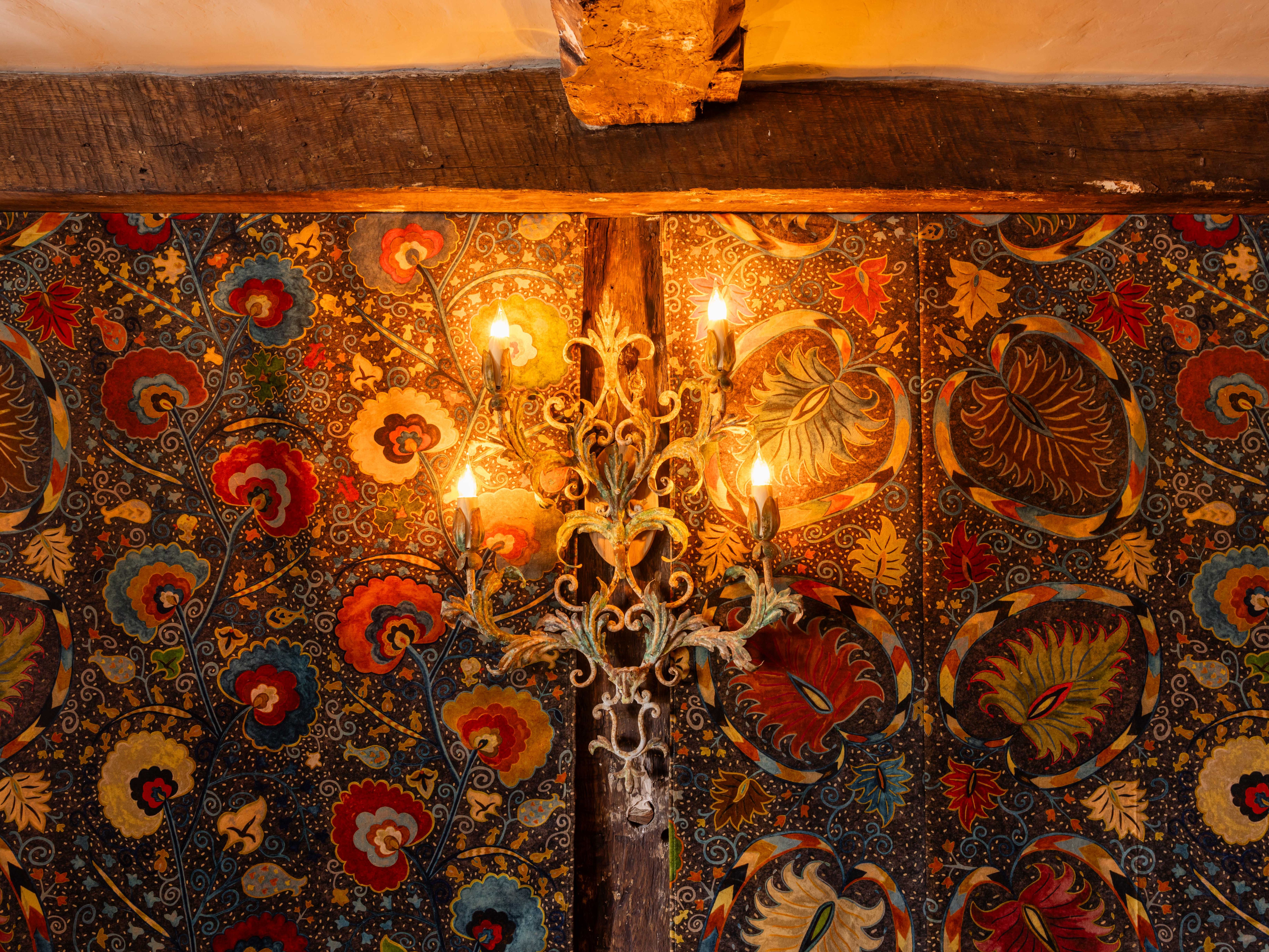 Ornate wall light fixture with exposed bulbs mounted on a colorful, floral-patterned wall