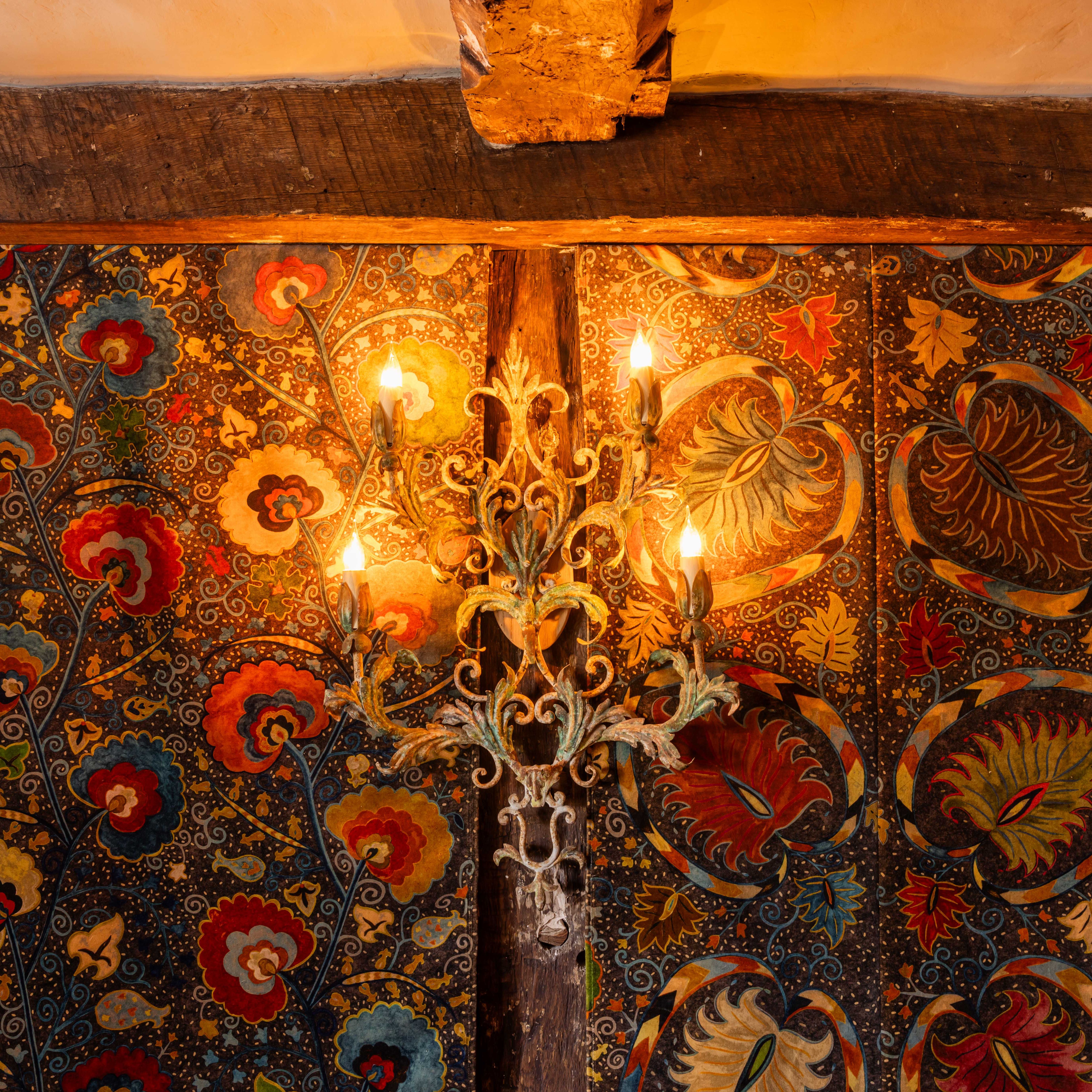Ornate wall light fixture with exposed bulbs mounted on a colorful, floral-patterned wall