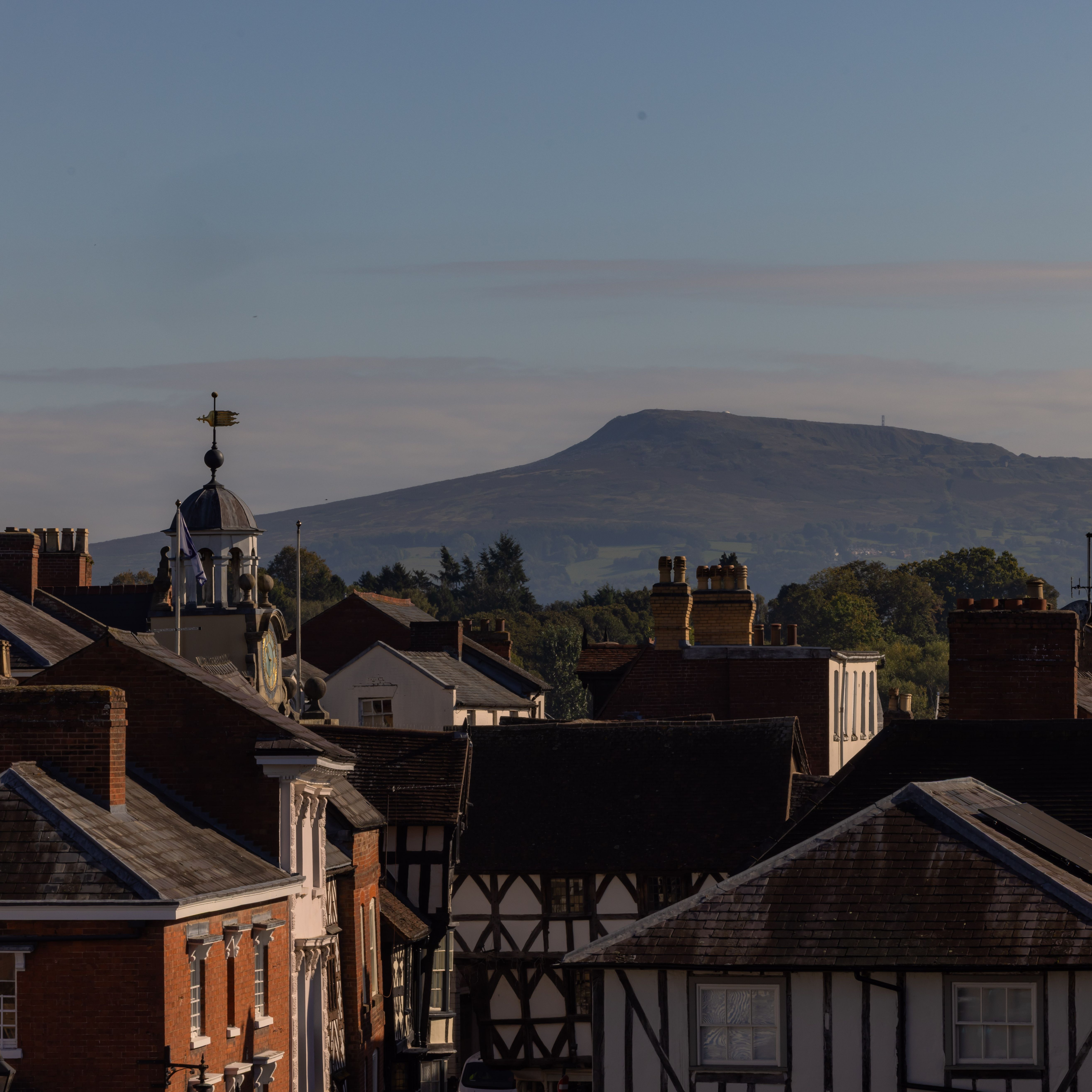 View of a historic town with rooftops and a large hill in the background under a clear sky
