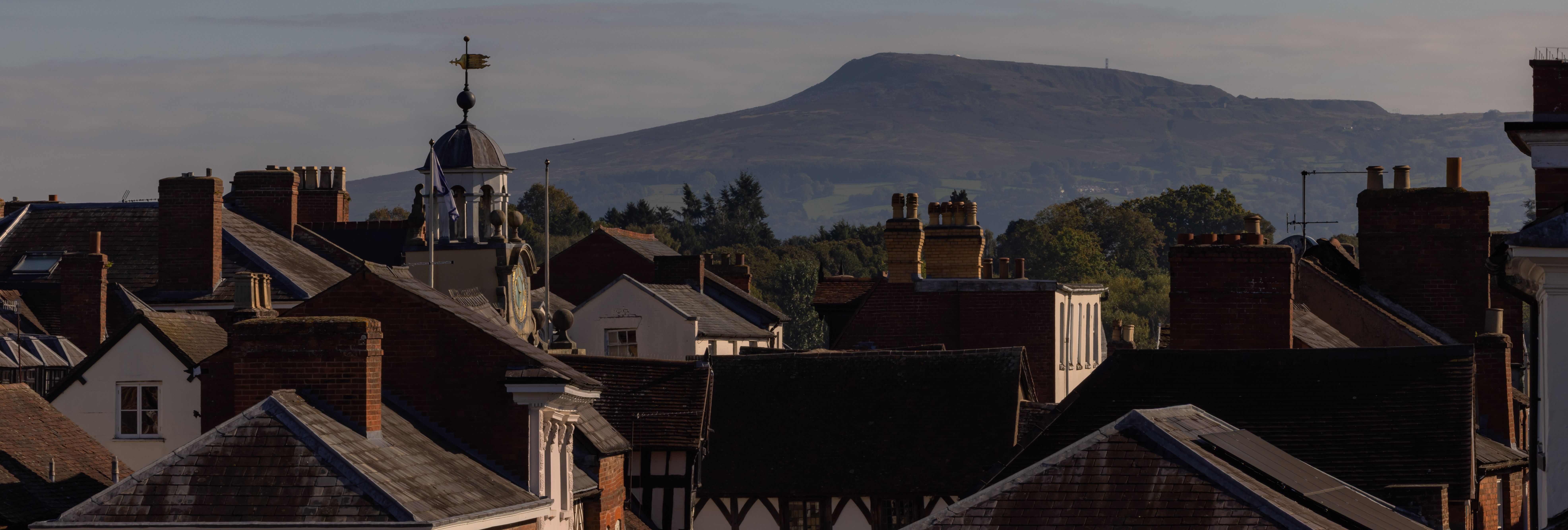 View of a historic town with rooftops and a large hill in the background under a clear sky