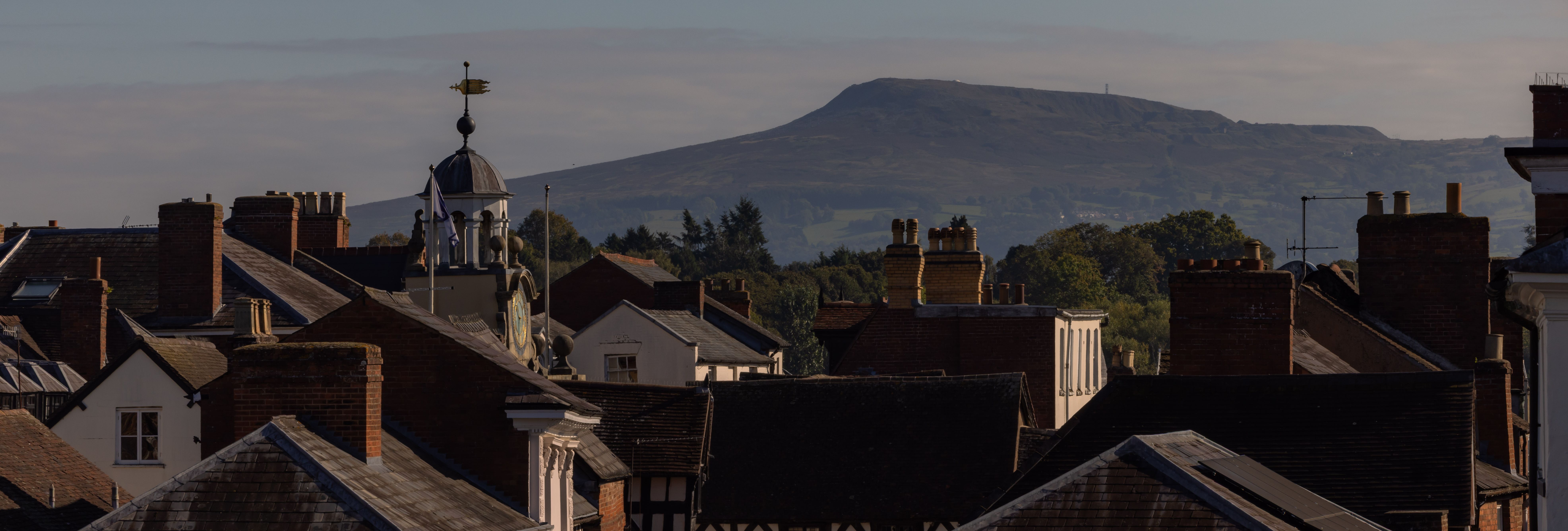 View of a historic town with rooftops and a large hill in the background under a clear sky