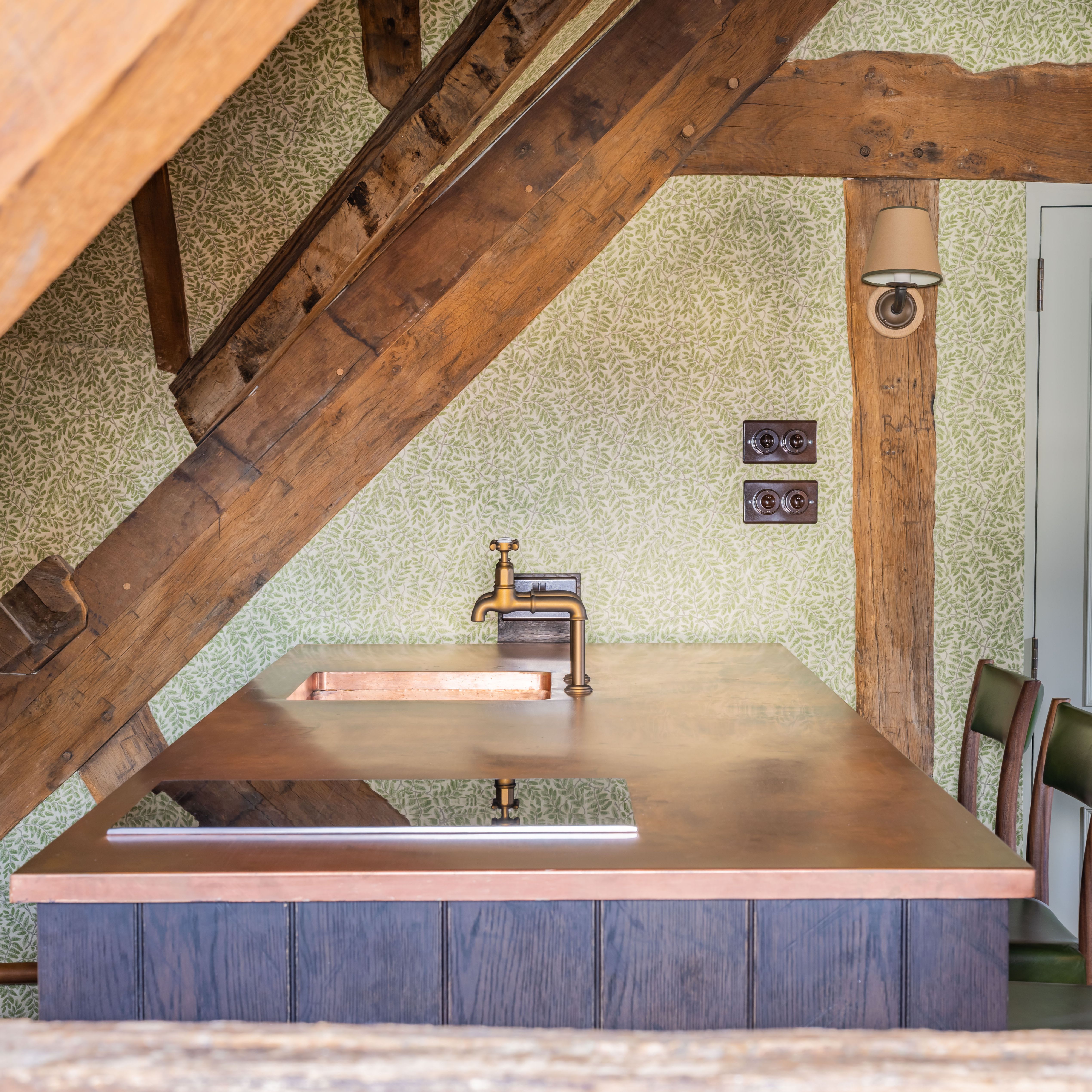 Rustic kitchen island with a copper countertop, brass faucet, and wooden beams