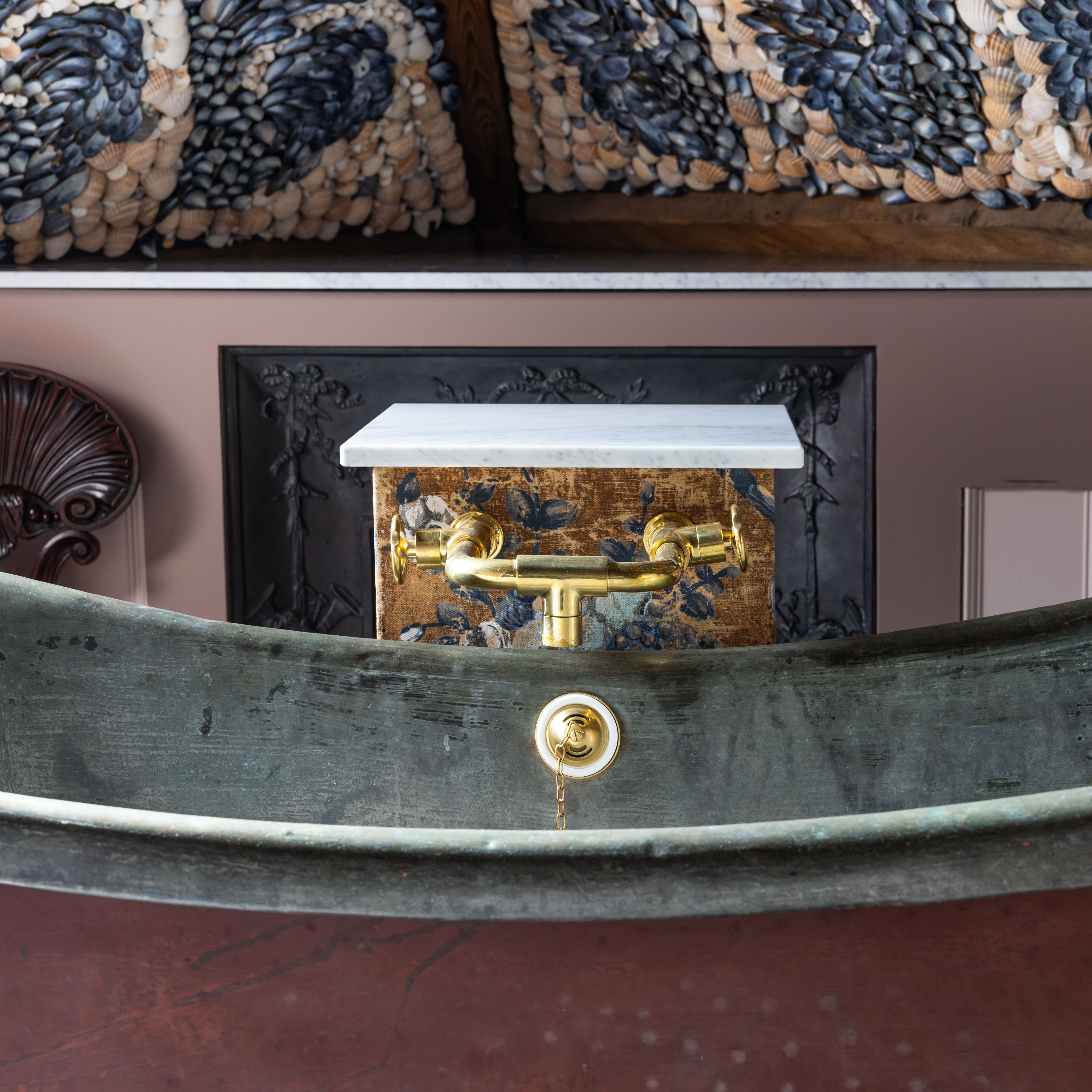 Vintage bathtub with brass fixtures, ornate shell mosaic ceiling, and decorative wall panel