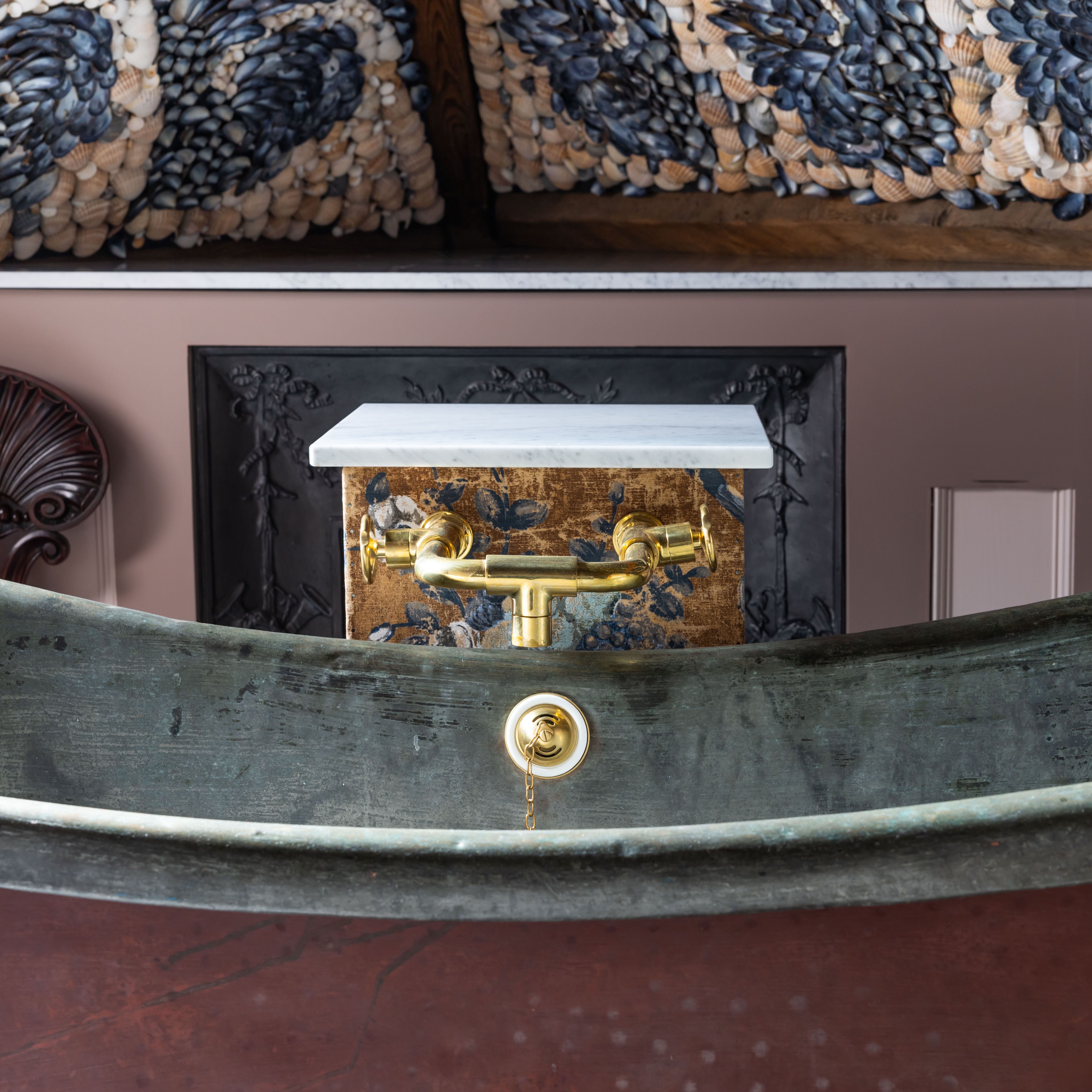 Vintage bathtub with brass fixtures, ornate shell mosaic ceiling, and decorative wall panel