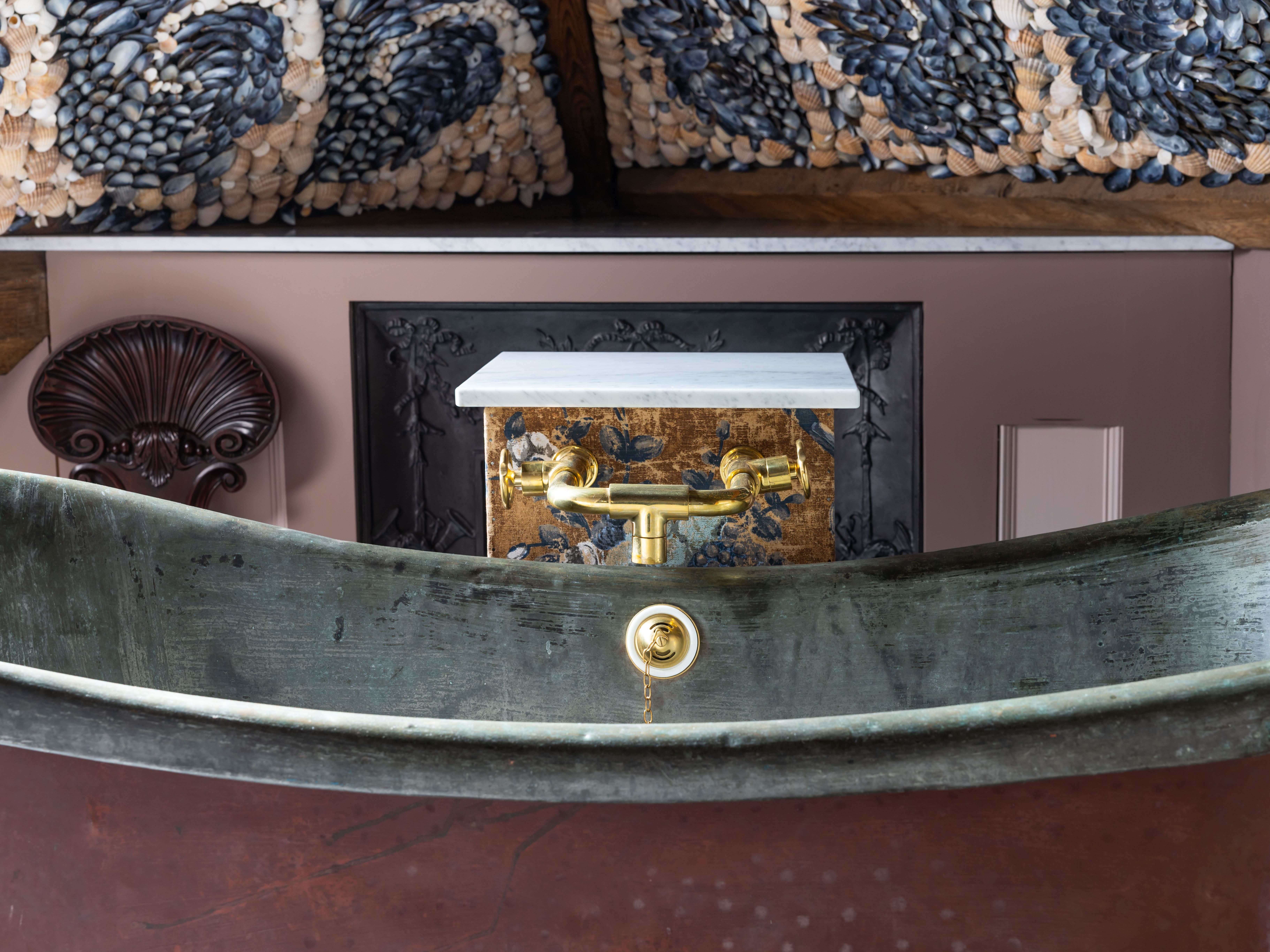 Vintage bathtub with brass fixtures, ornate shell mosaic ceiling, and decorative wall panel