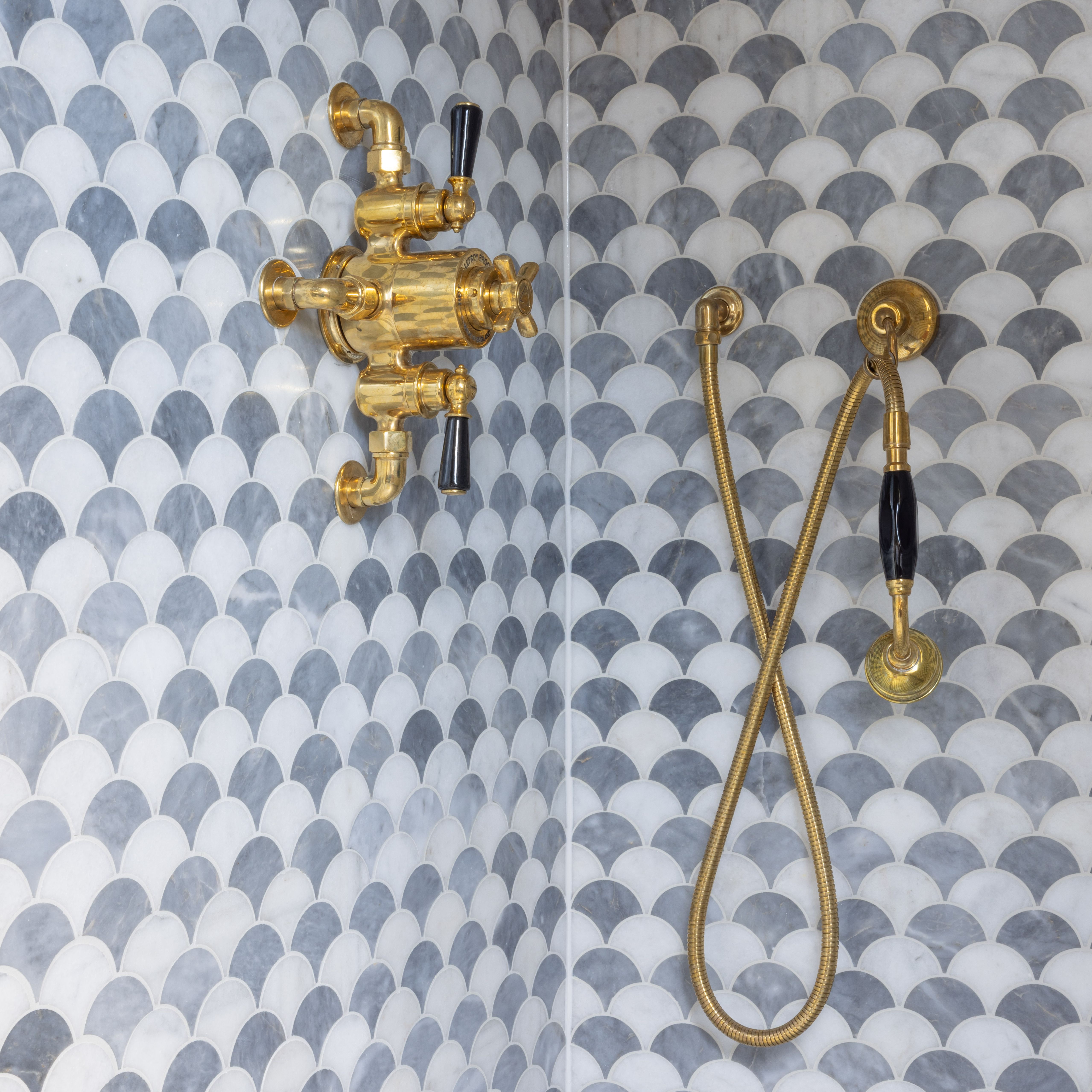 Shower with gold fixtures and scalloped marble tile walls