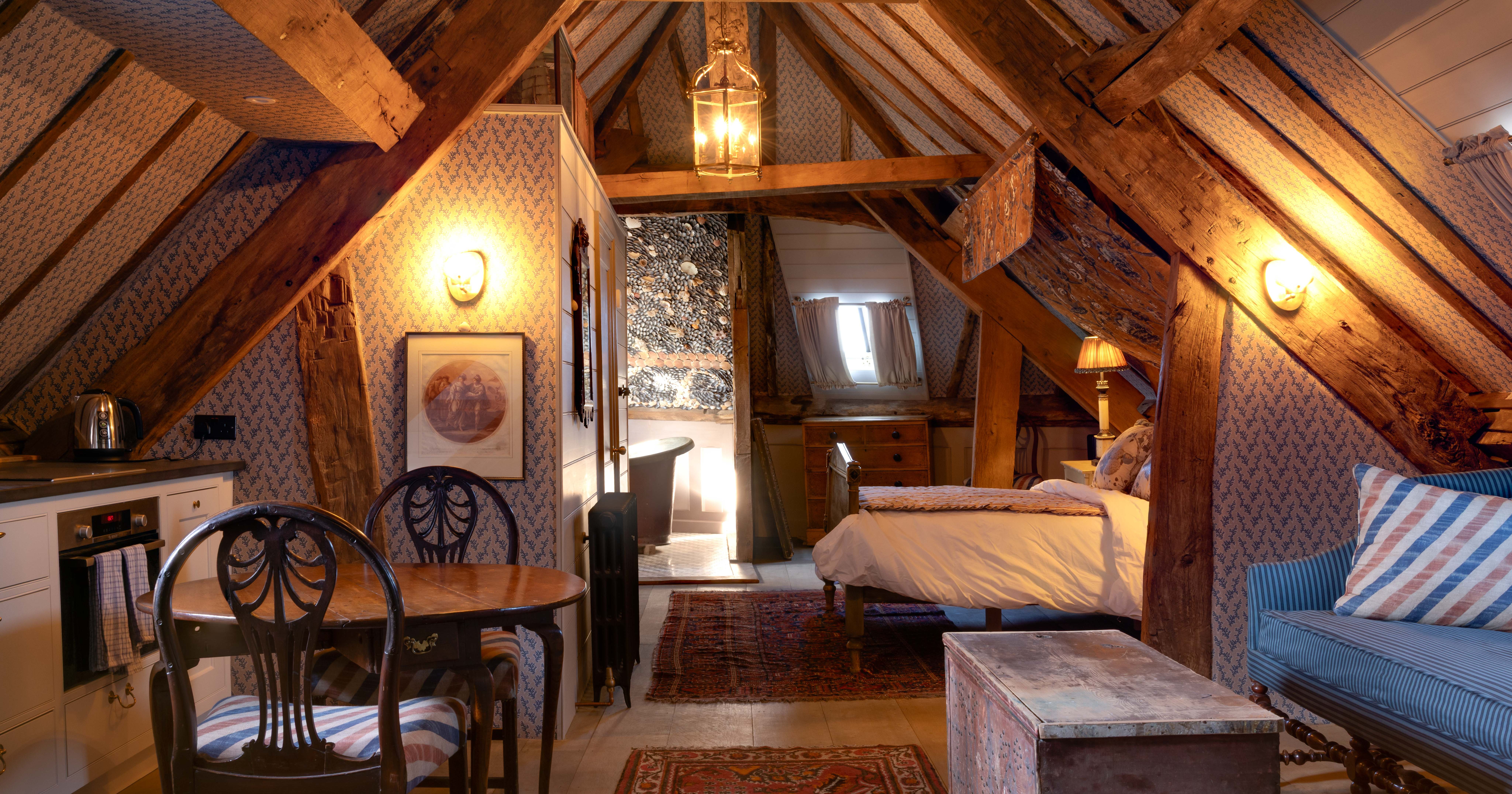 Cozy attic suite with exposed wooden beams, a bed, sitting area, small dining table and kitchenette.
