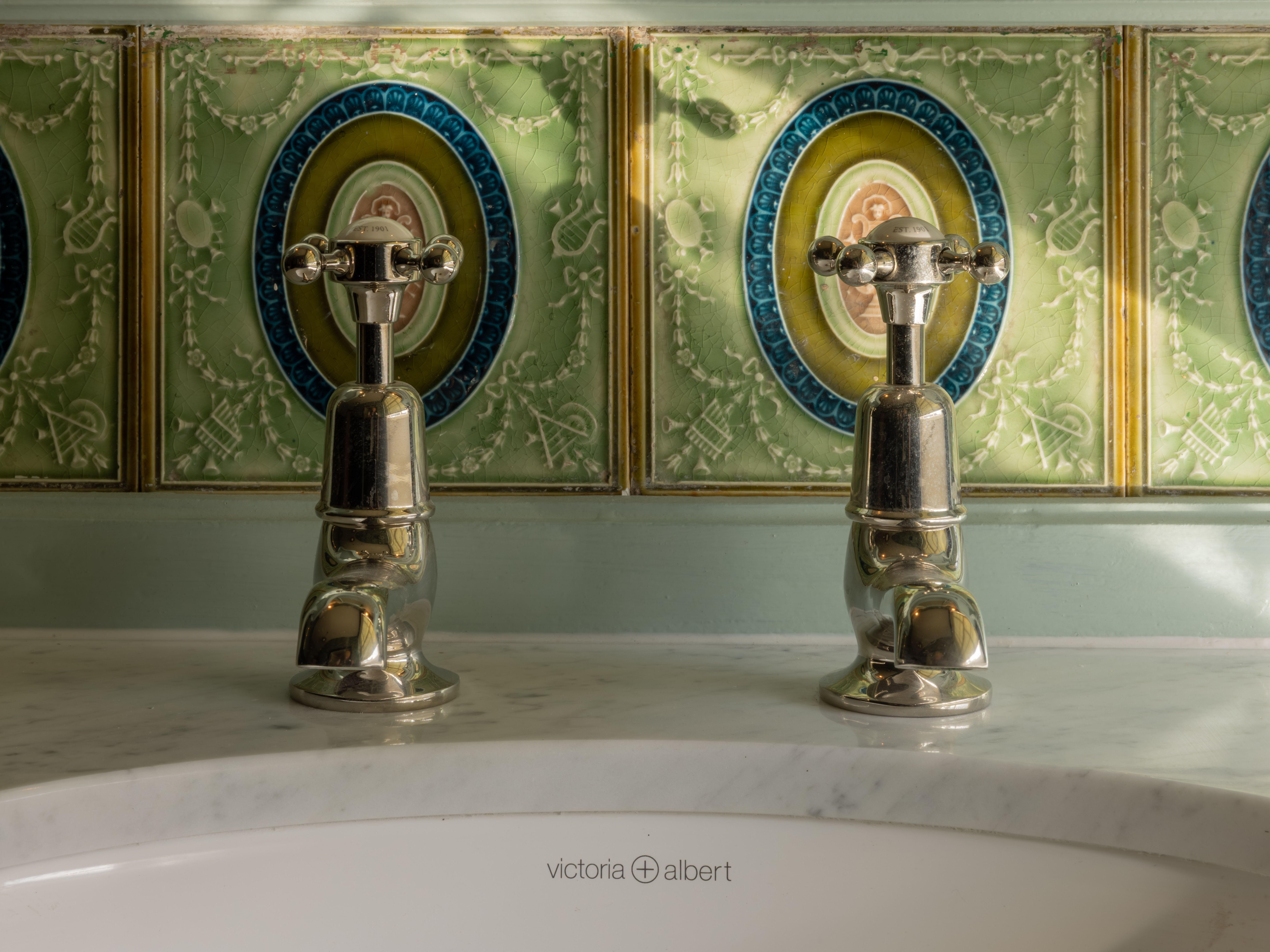 Victorian-style bathroom sink with two chrome faucets and ornate green decorative tiles