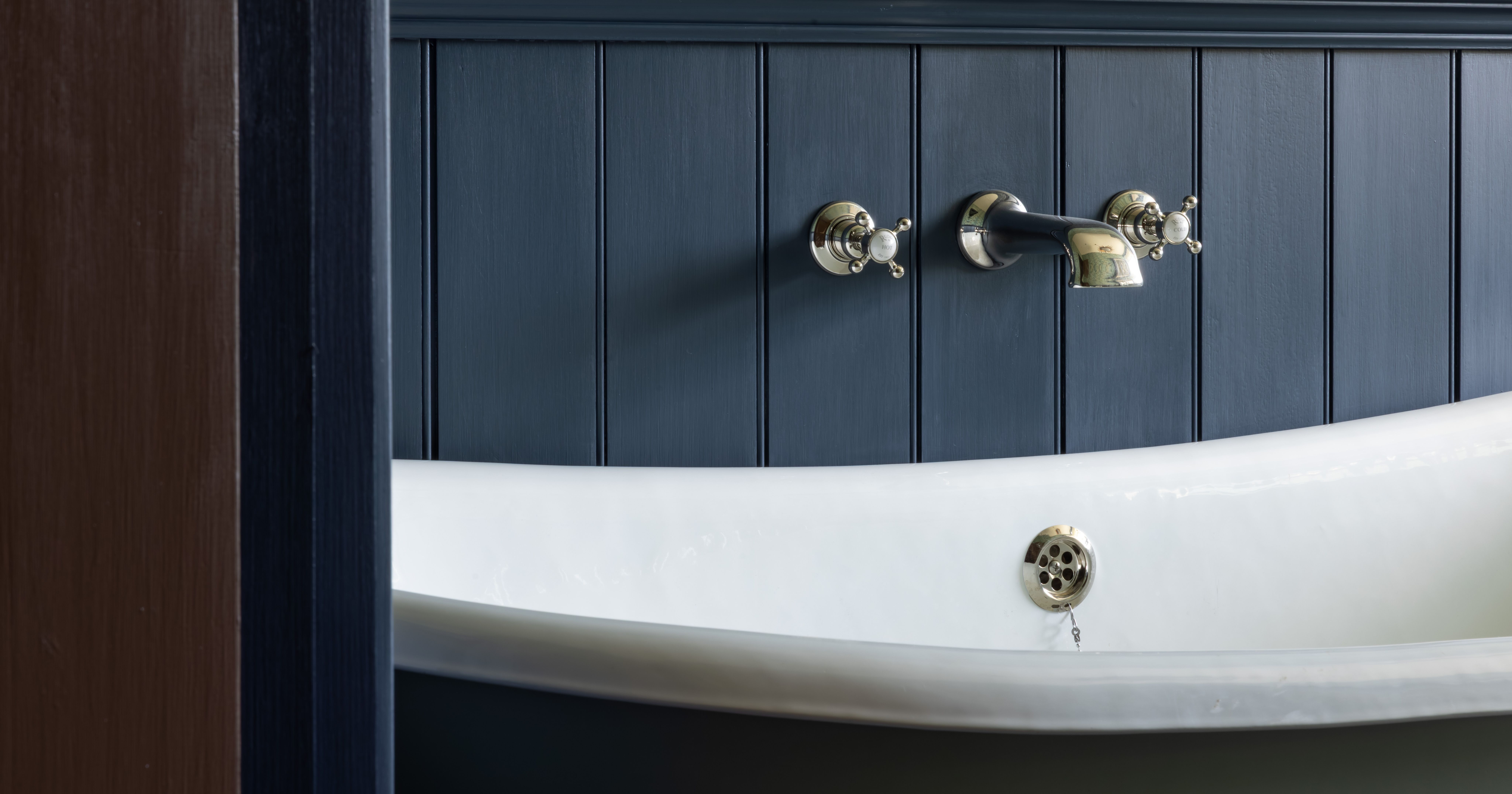 Close-up of a Victorian-style bathtub with vintage chrome fixtures against navy paneling and floral wallpaper.
