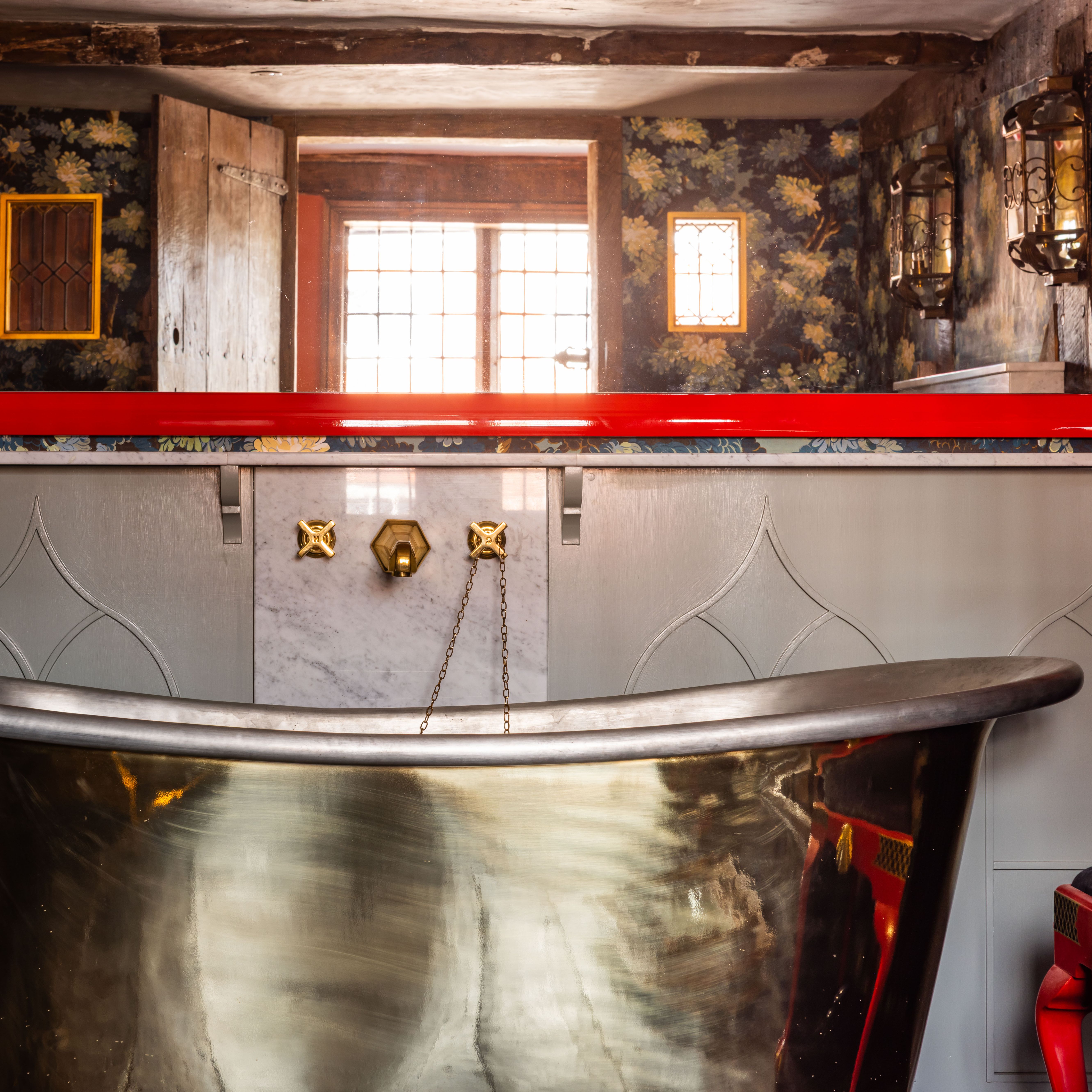 Luxurious bathroom with a metallic bathtub, decorative wallpaper, and vintage fixtures