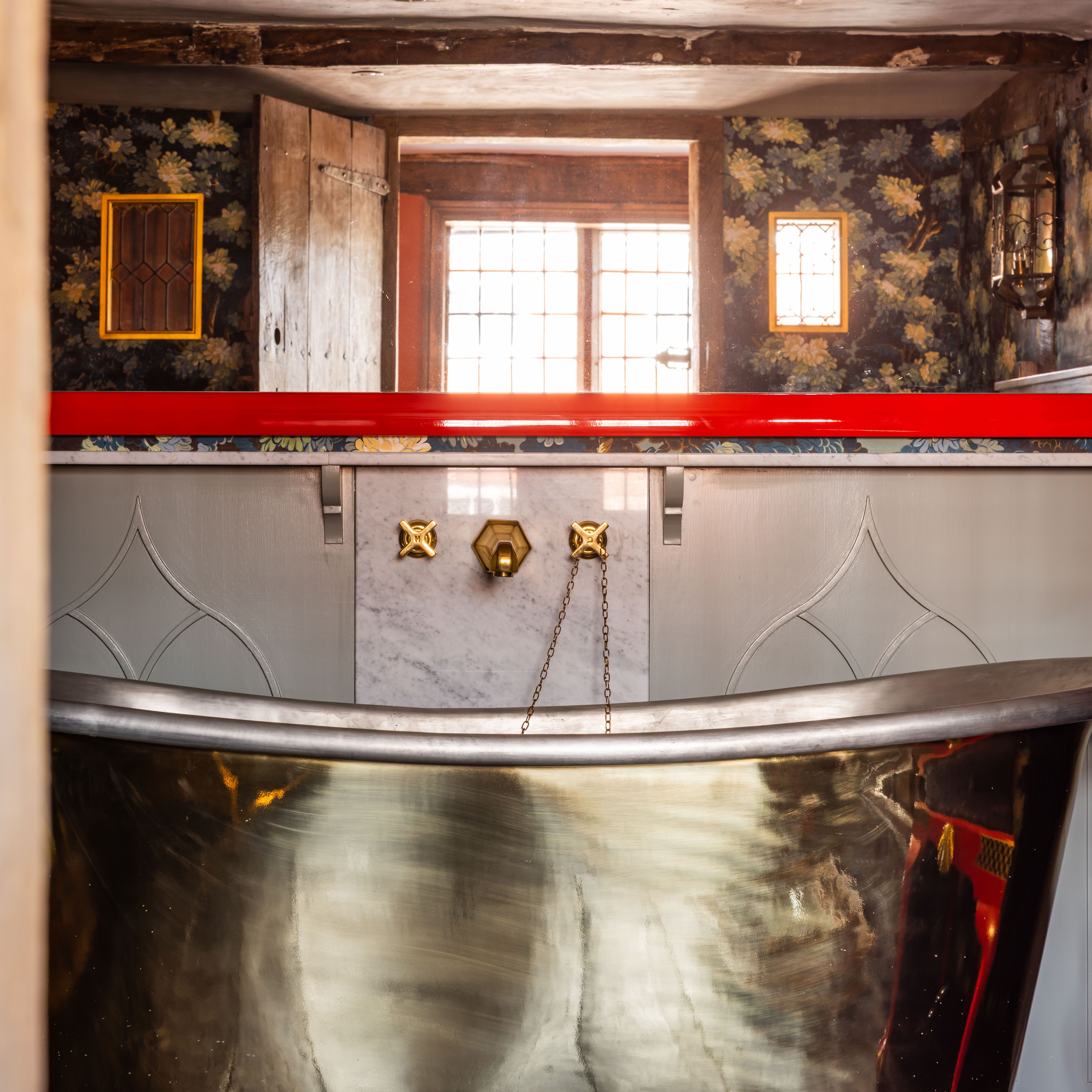 Luxurious bathroom with a metallic bathtub, decorative wallpaper, and vintage fixtures