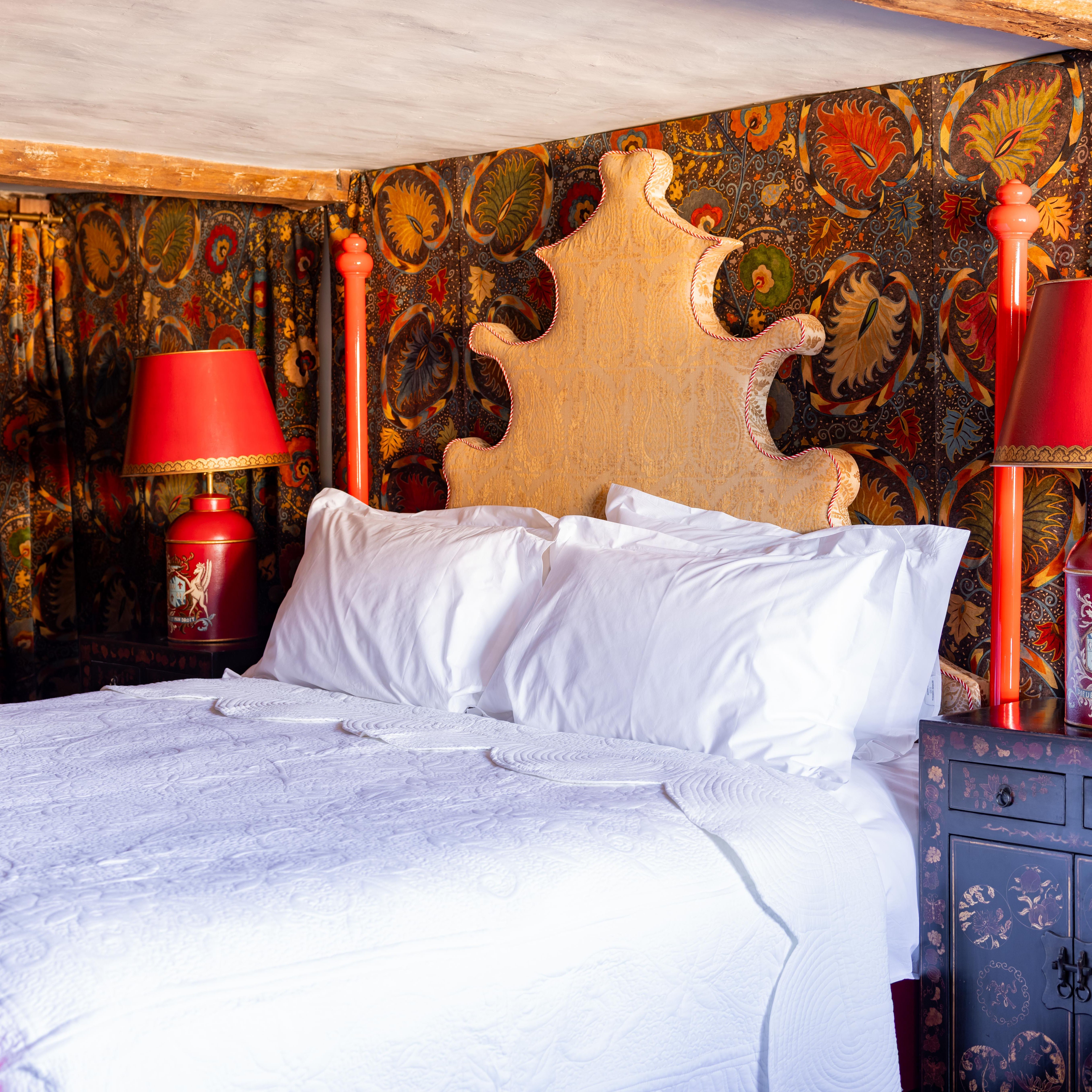 Ornate bedroom with a four-poster bed, colorful patterned drapes, red lamps and a unique headboard