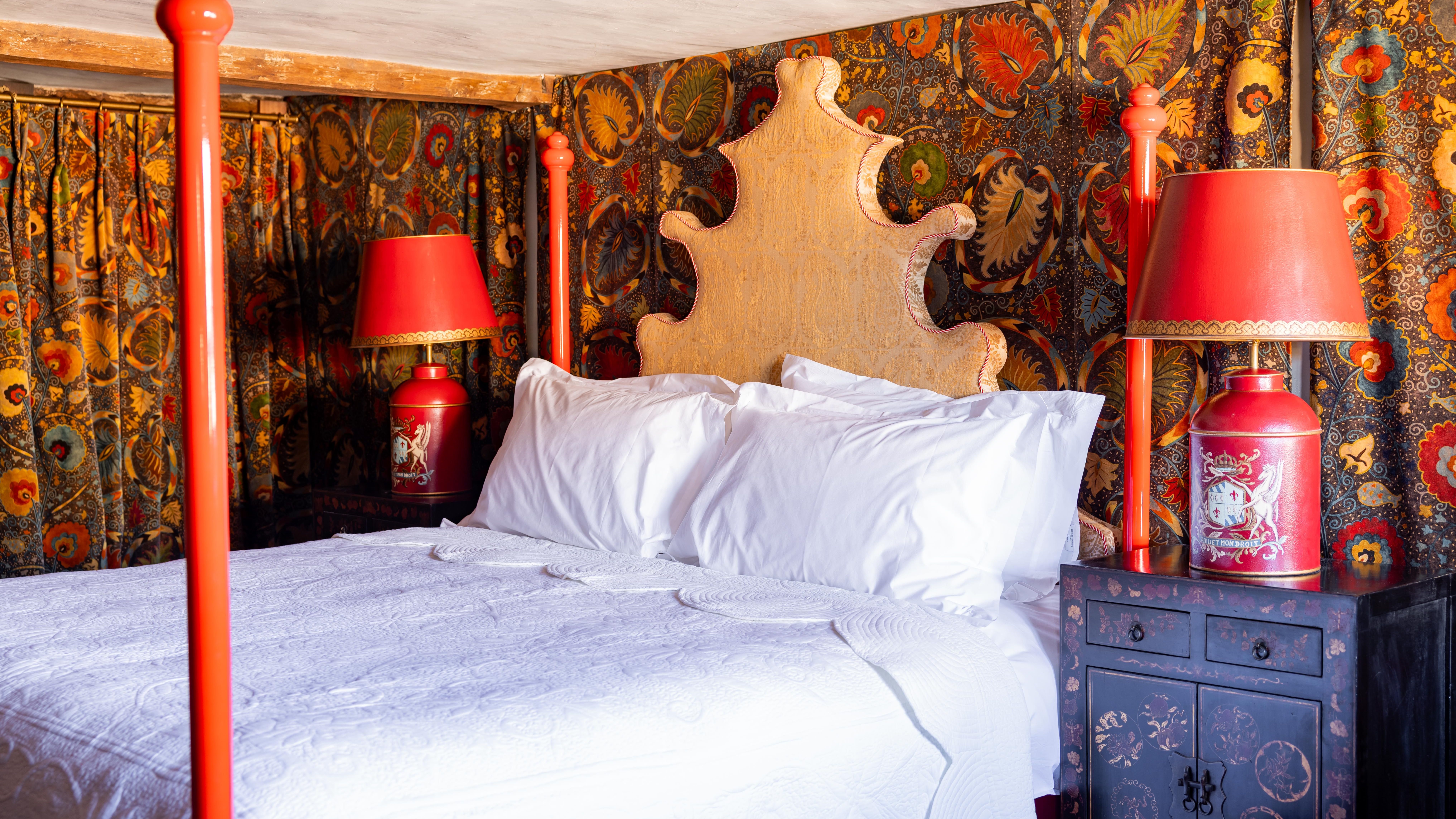 Ornate bedroom with a four-poster bed, colorful patterned drapes, red lamps and a unique headboard