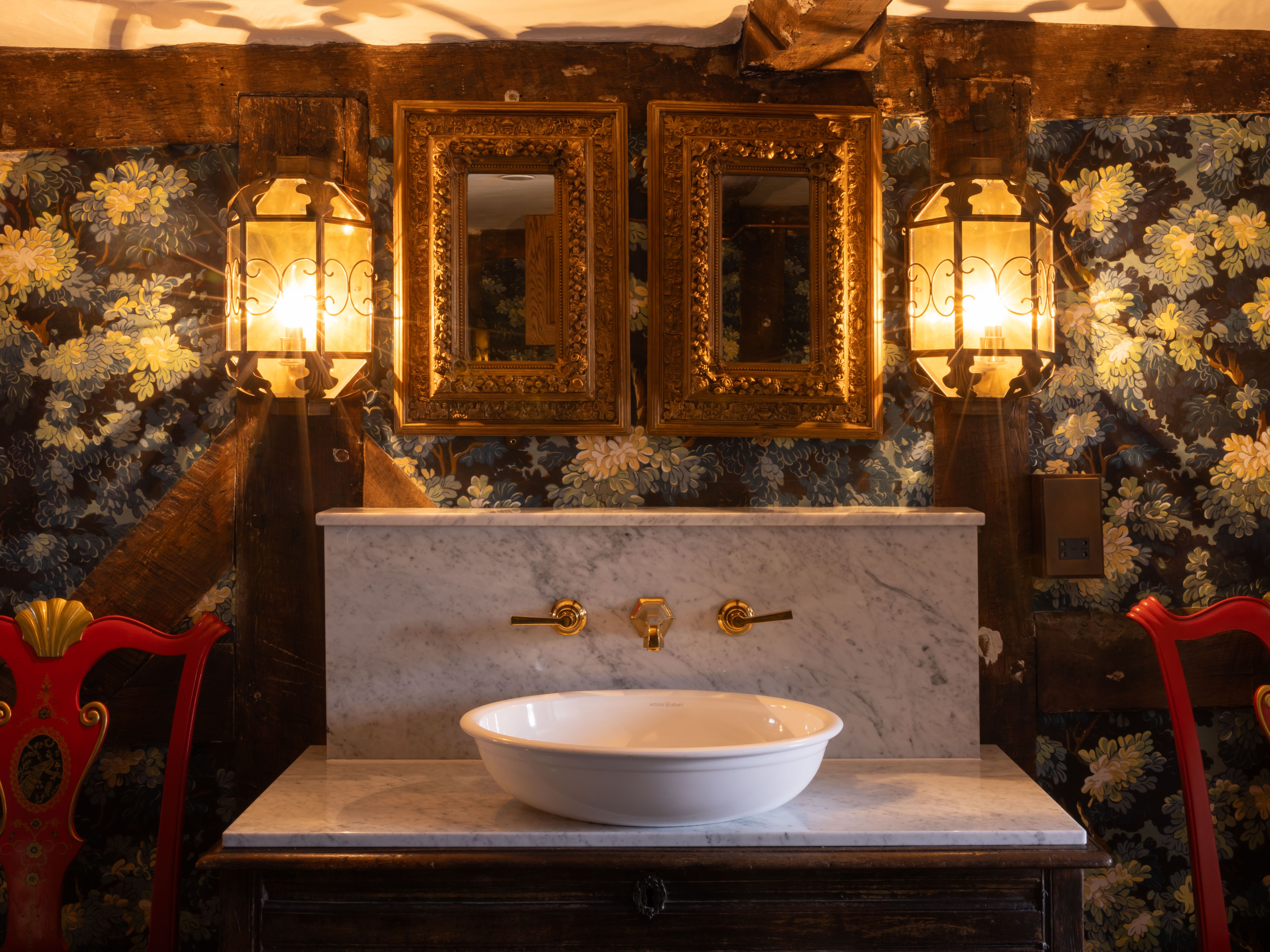 Elegant vintage sink setup in a historic bedroom with floral wallpaper, ornate mirrors, and gold fixtures.
