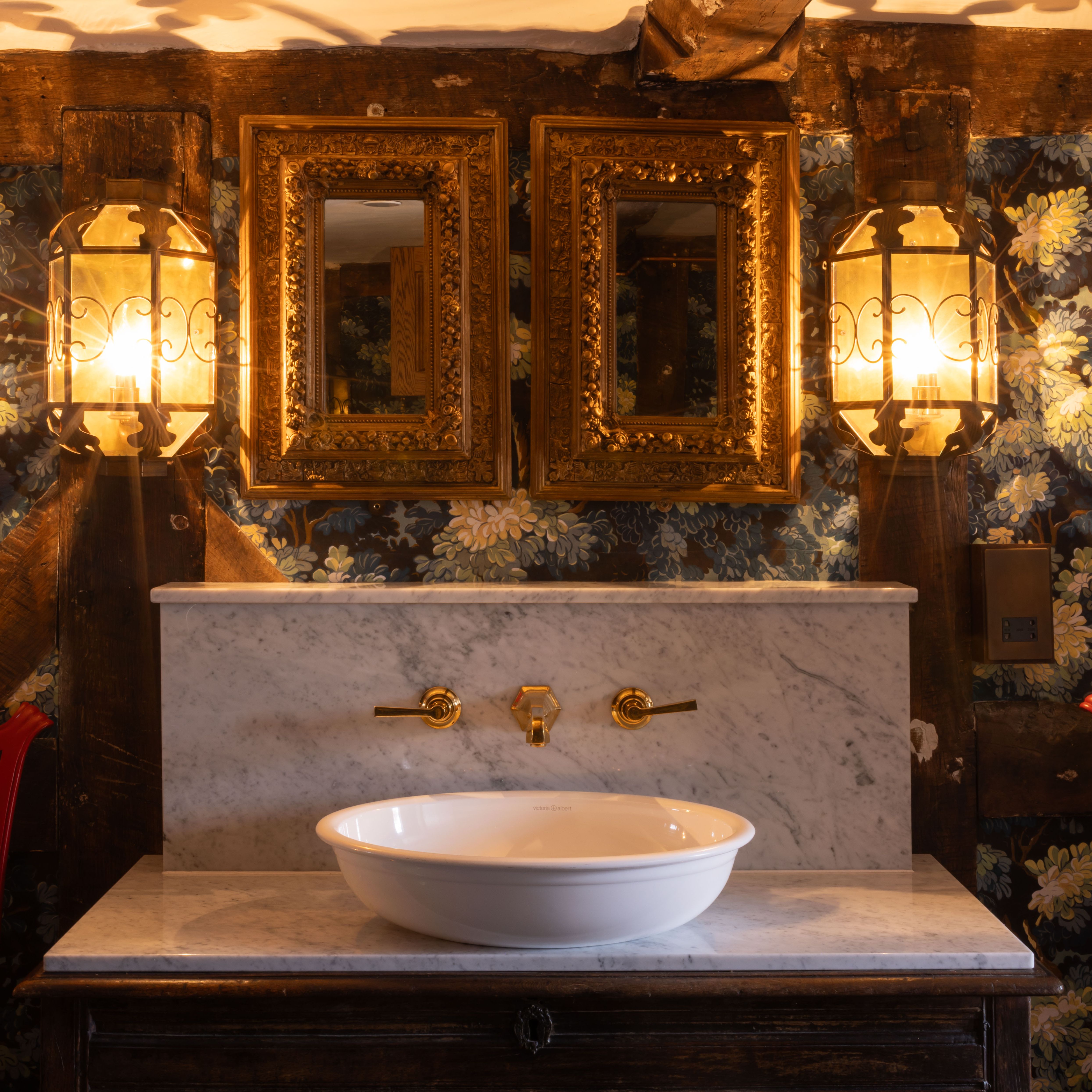 Elegant vintage sink setup in a historic bedroom with floral wallpaper, ornate mirrors, and gold fixtures.