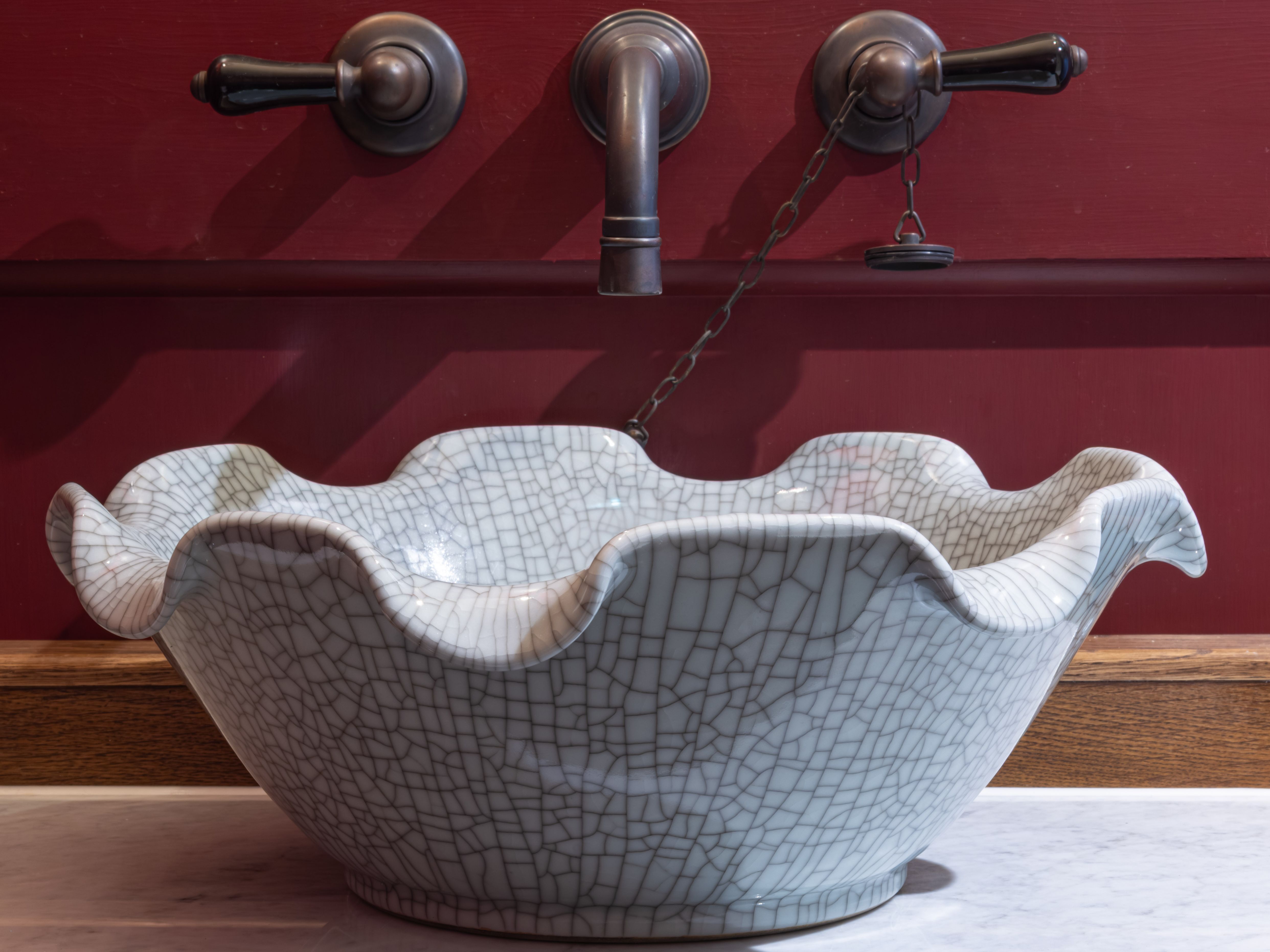Decorative ceramic bathroom sink with a ruffled edge and crackle glaze finish, set on a marble countertop with vintage faucet fixtures.