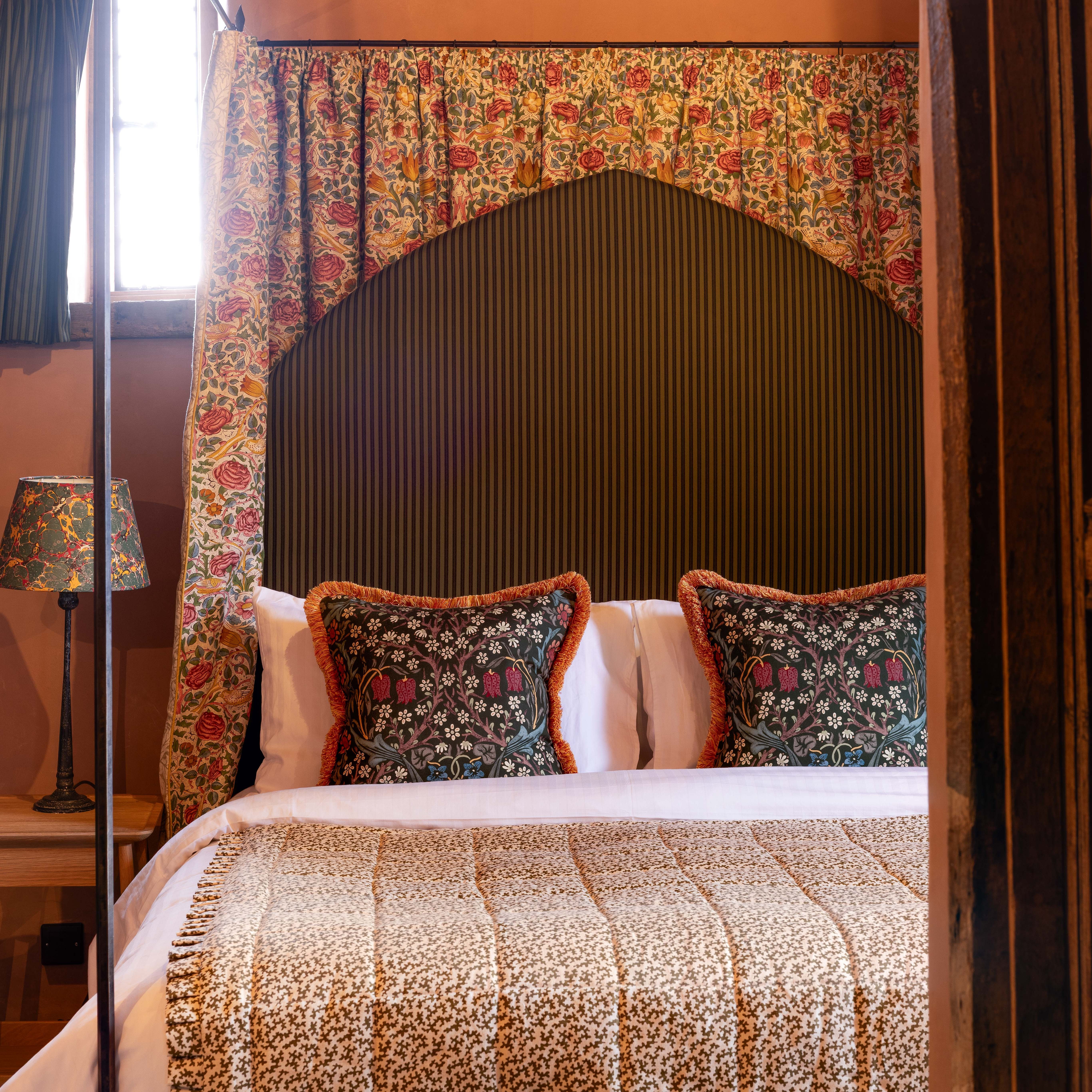 Cozy bed with patterned floral pillows, a matching bedspread, and floral curtains with a vintage lamp beside the bed.