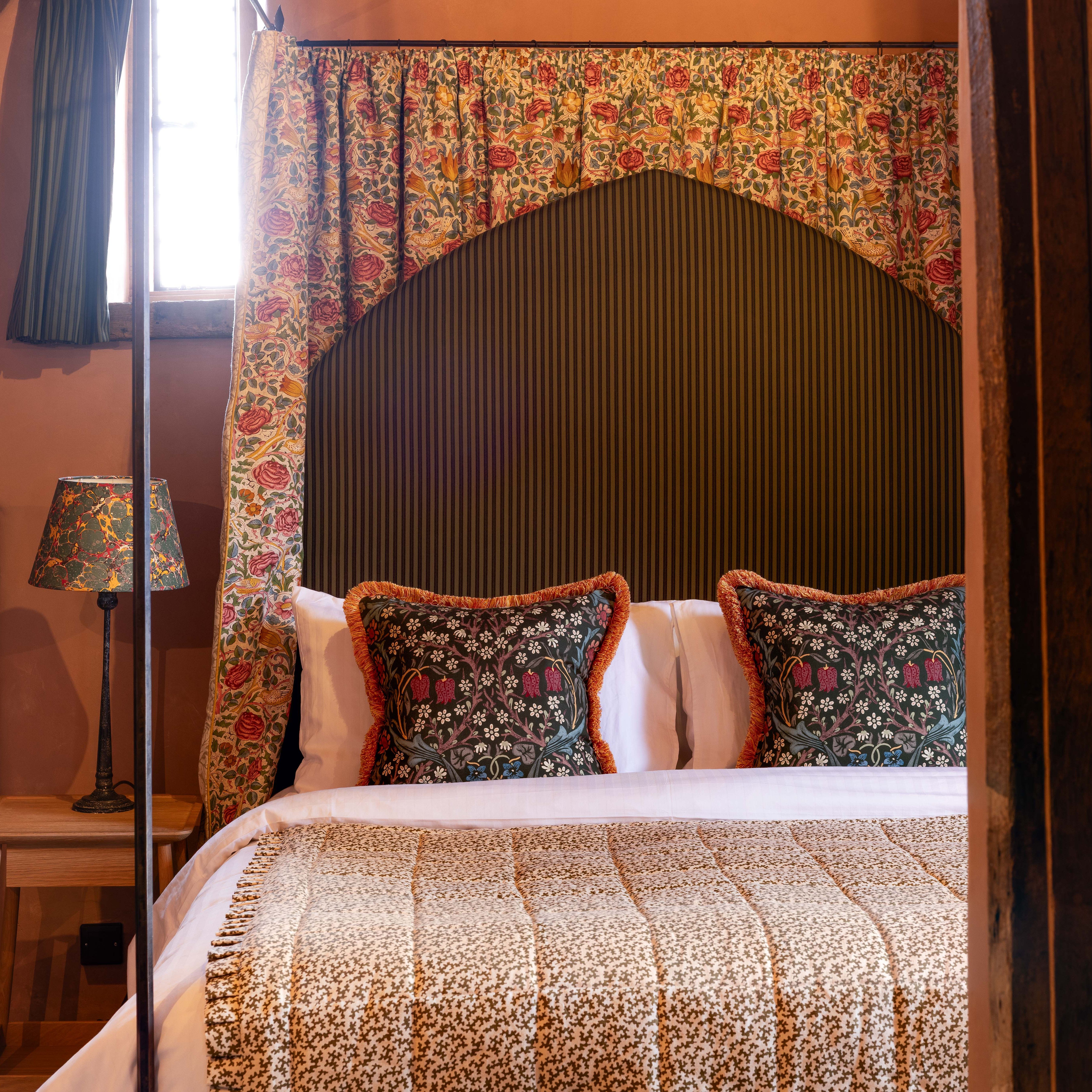 Cozy bed with patterned floral pillows, a matching bedspread, and floral curtains with a vintage lamp beside the bed.