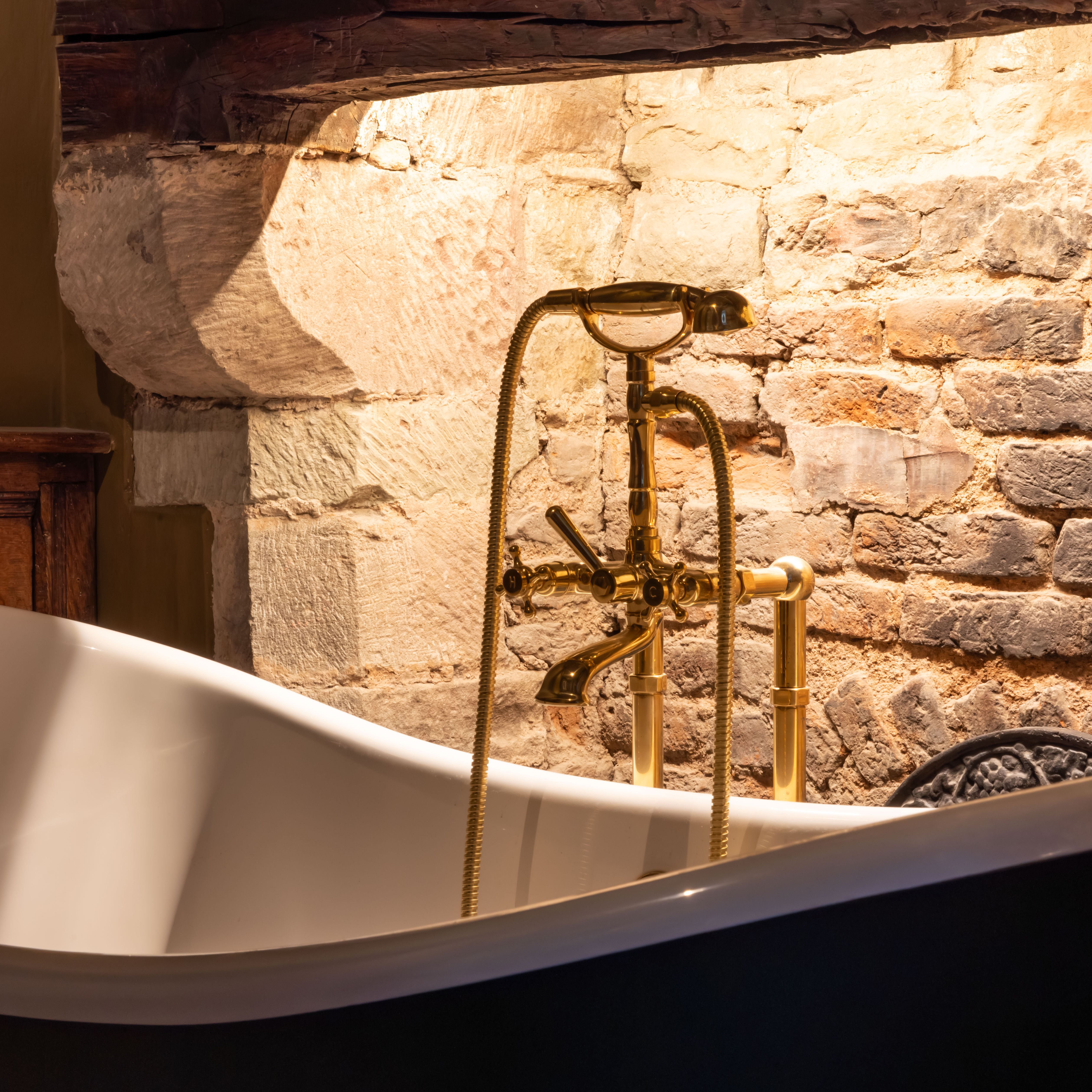 Vintage bathtub with gold faucet in front of exposed brick wall and rustic wood mantel