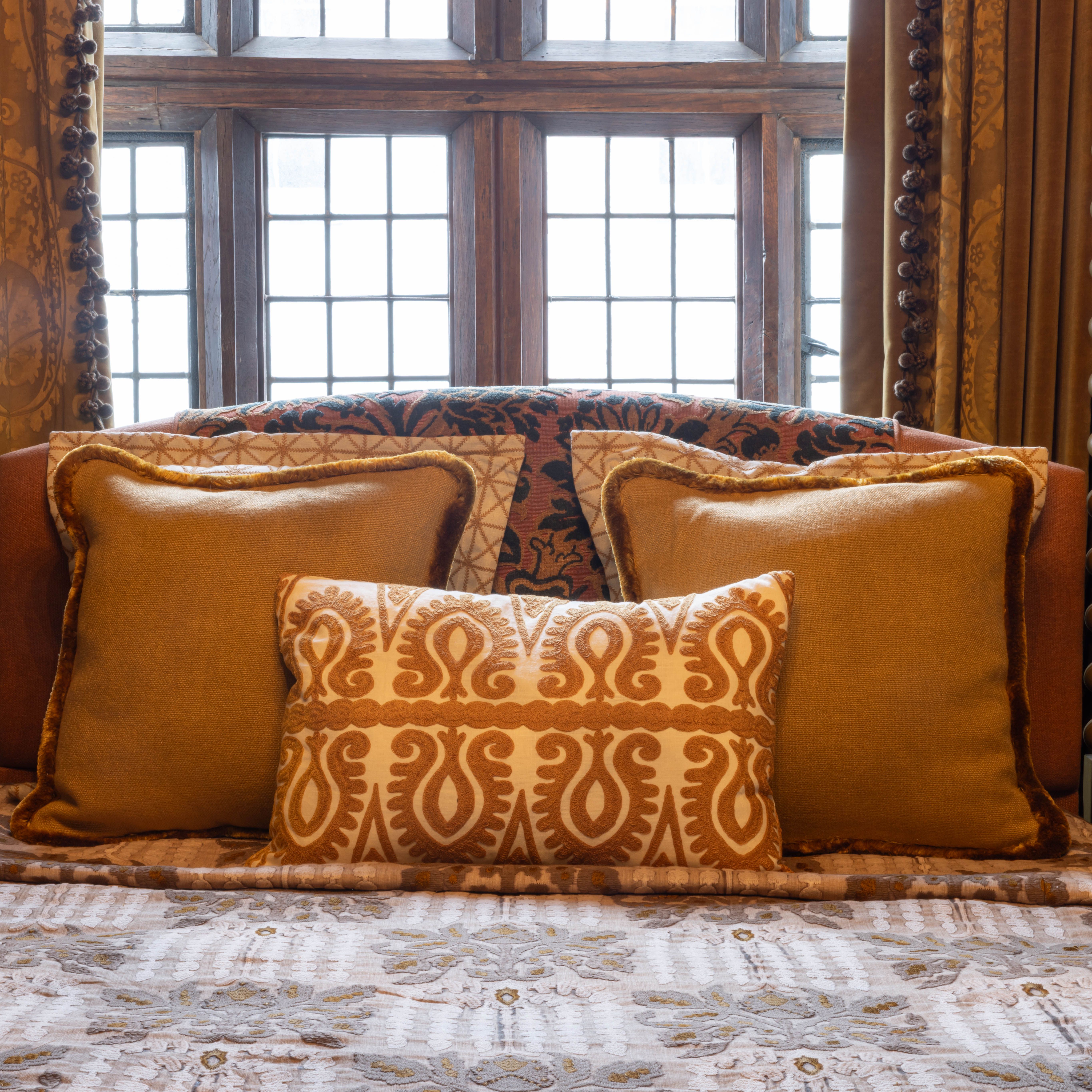 Close up of a luxurious bed with ornate pillows and an antique wooden headboard set against a leaded glass window.