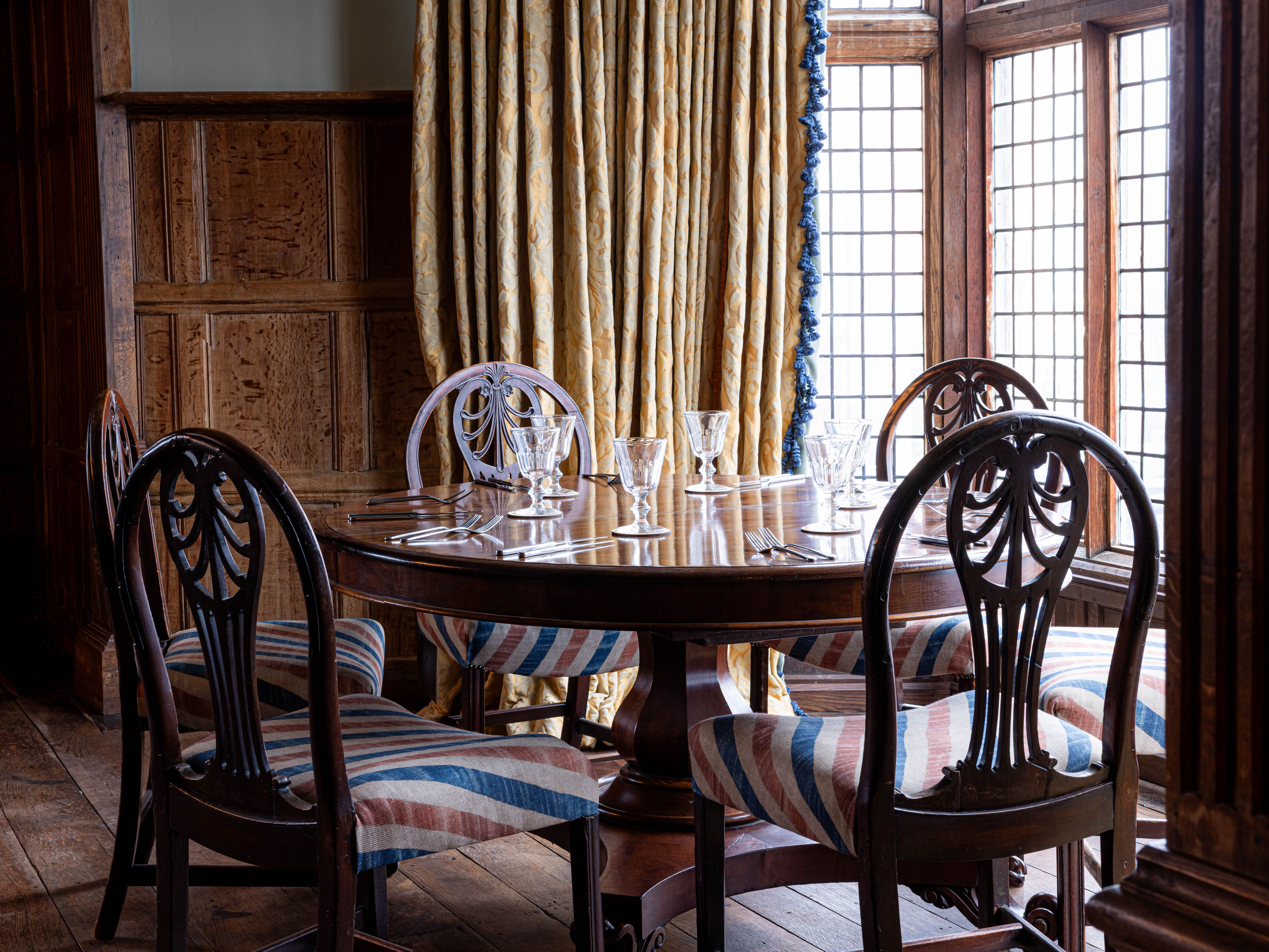 Elegant wooden dining table set with glassware in a classic room with wood-paneled walls and large windows