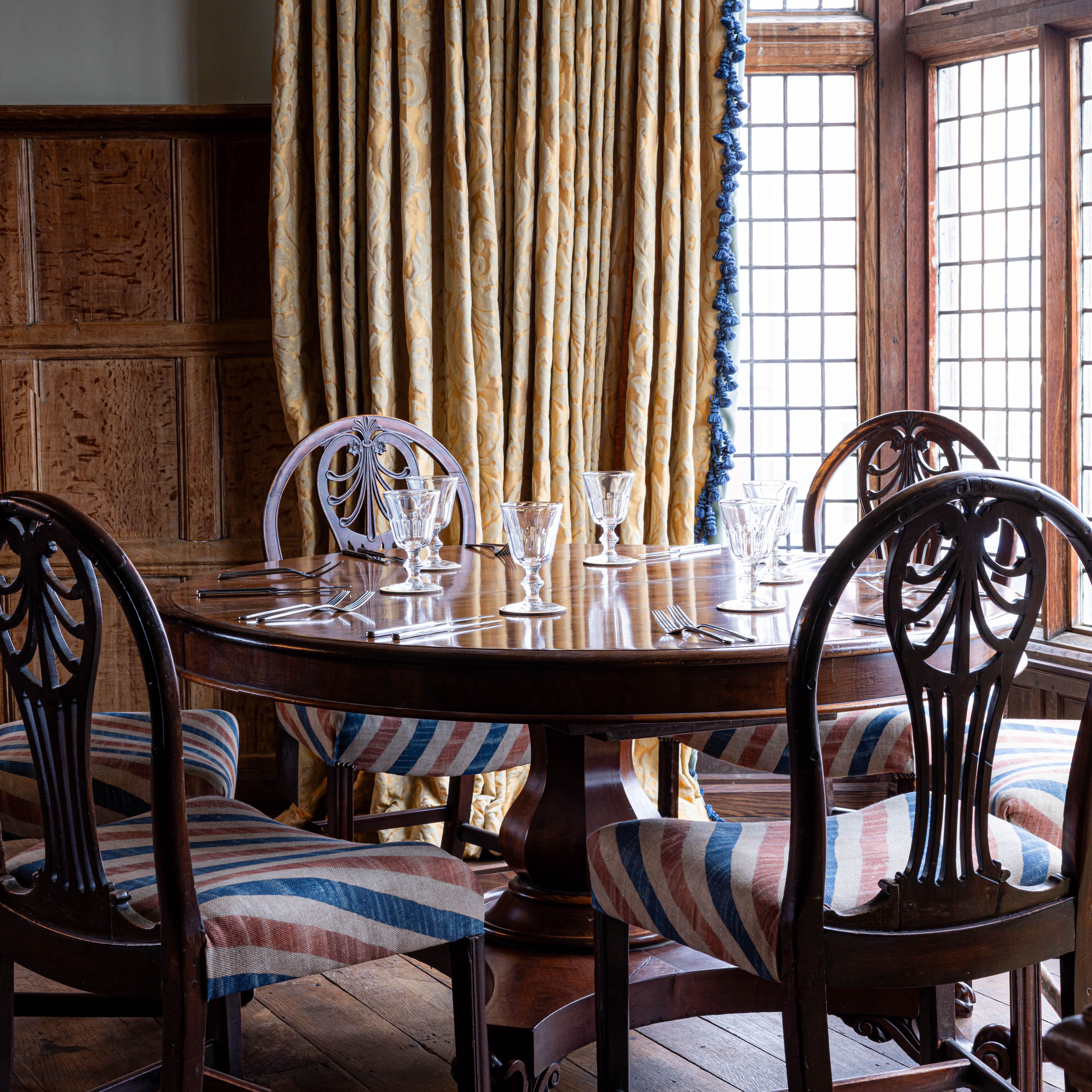 Elegant wooden dining table set with glassware in a classic room with wood-paneled walls and large windows