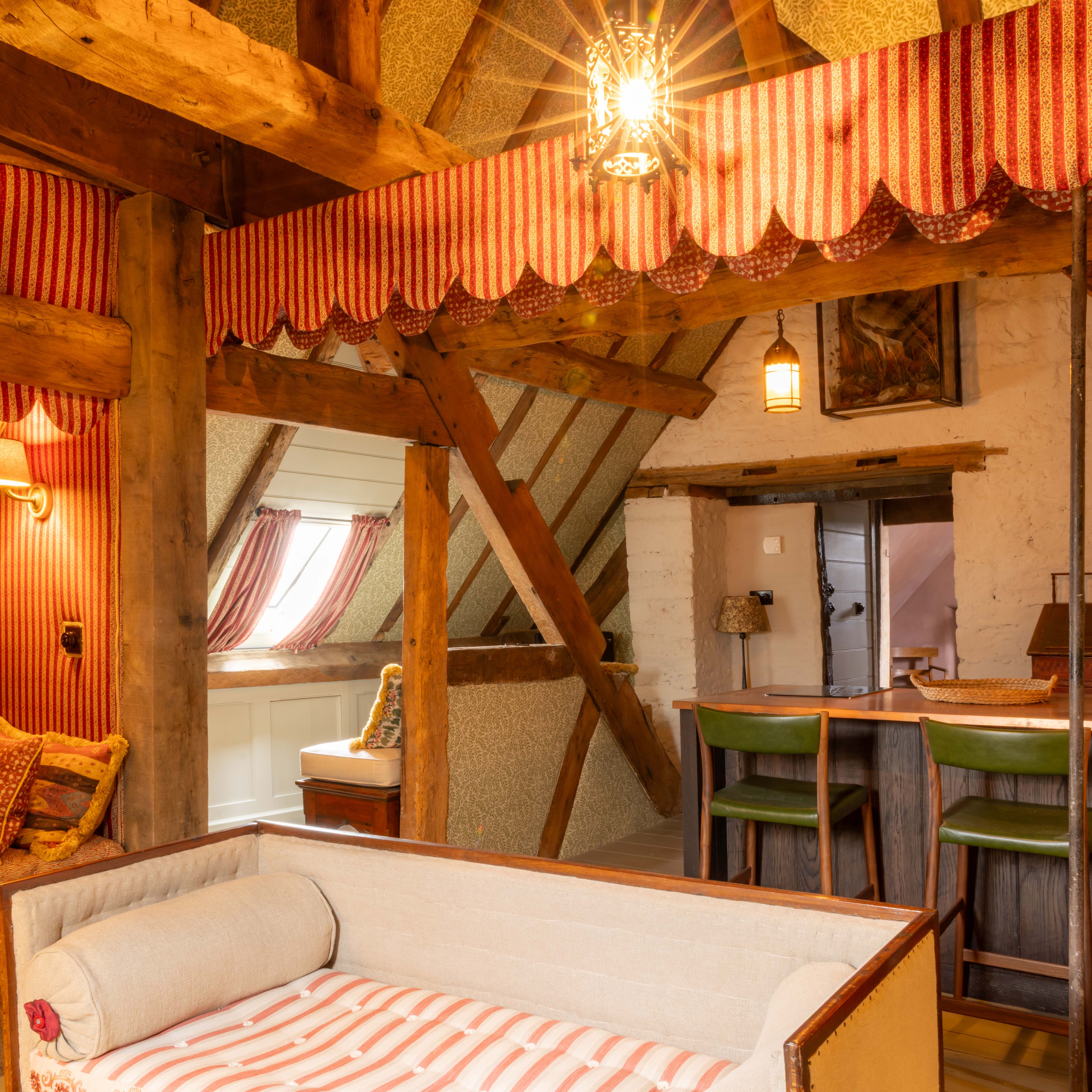 Cozy attic lounge with rustic wooden beams, striped red curtains, and bar seating