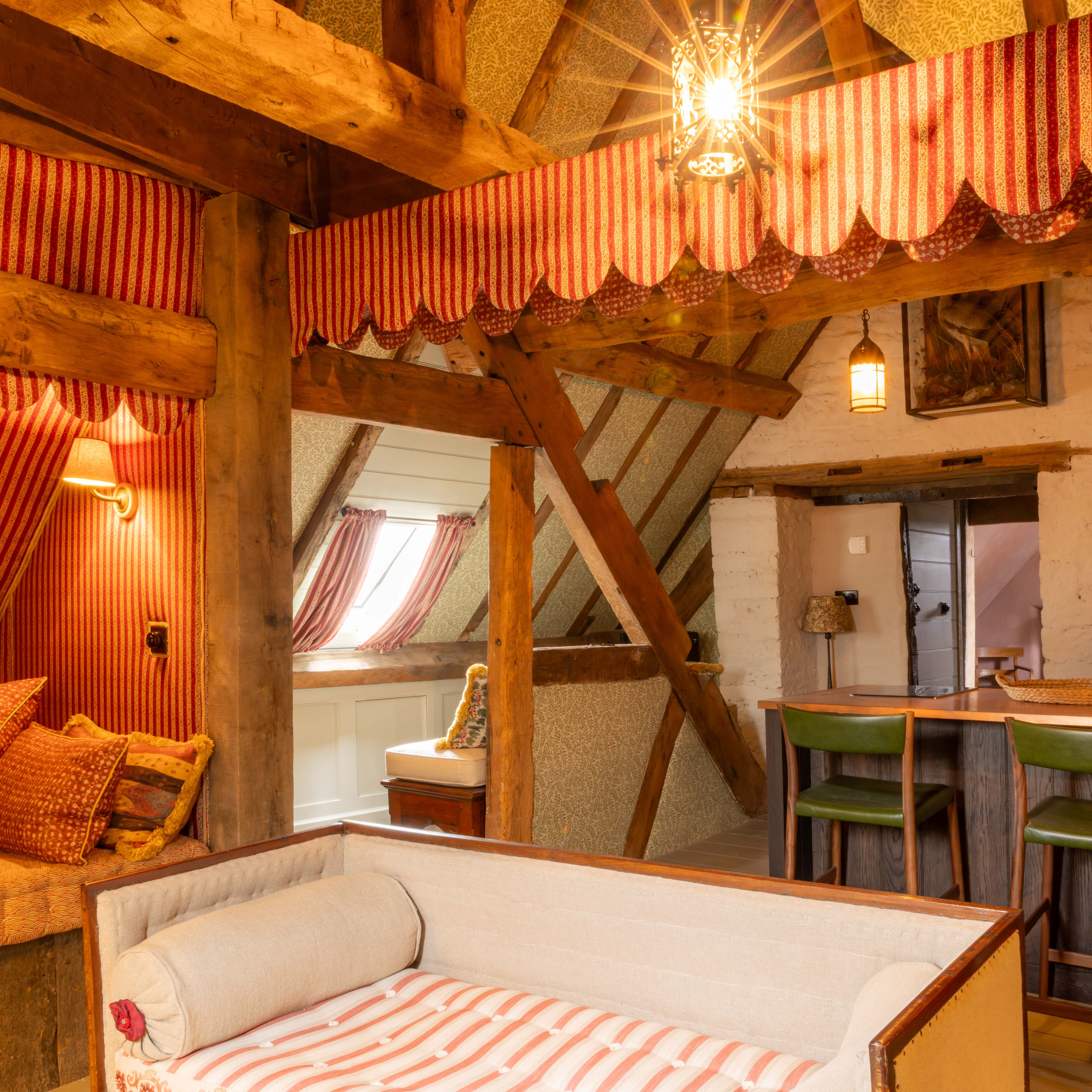 Cozy attic lounge with rustic wooden beams, striped red curtains, and bar seating