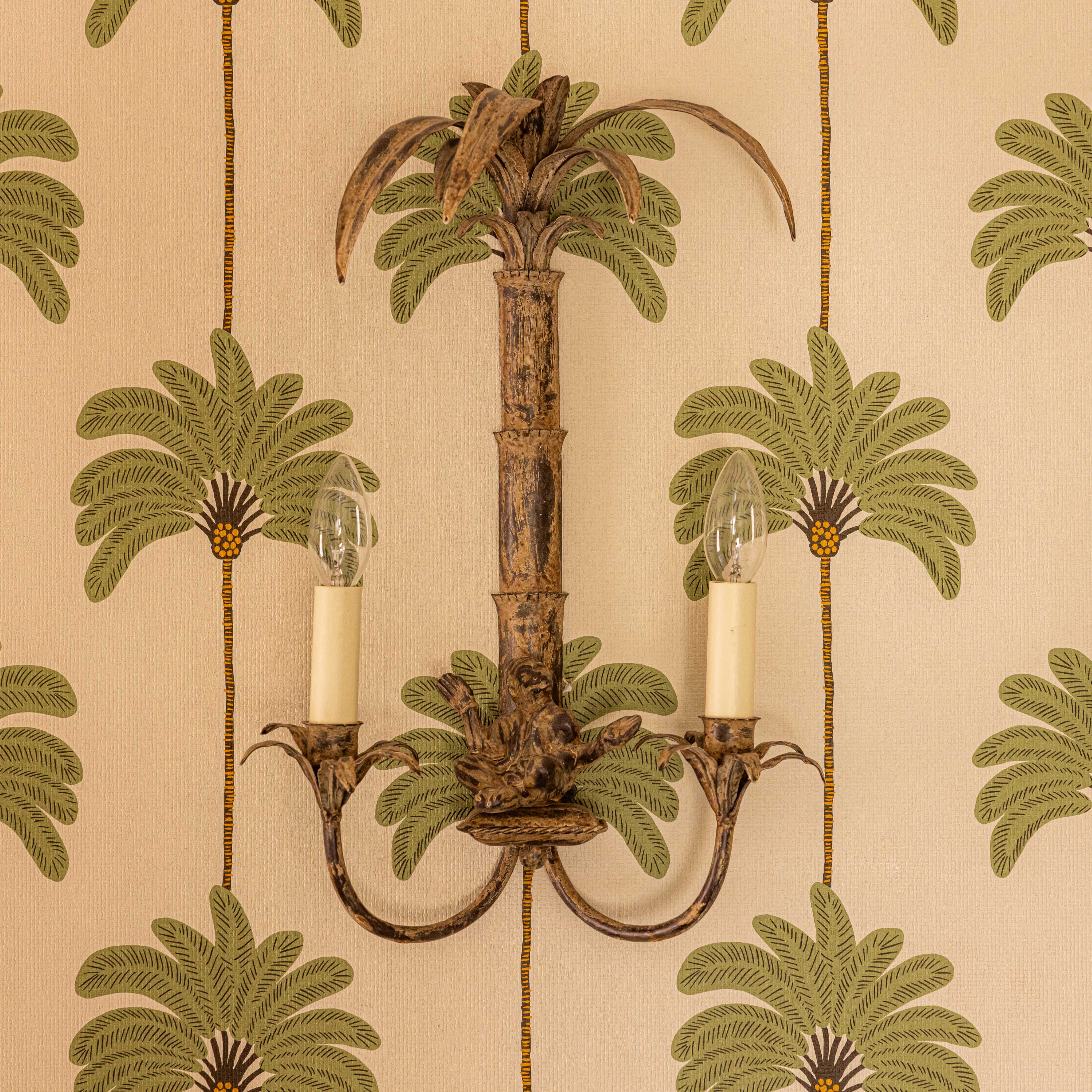 Victorian style wall light fixture mounted on a wall with tropical palm tree pattern wallpaper