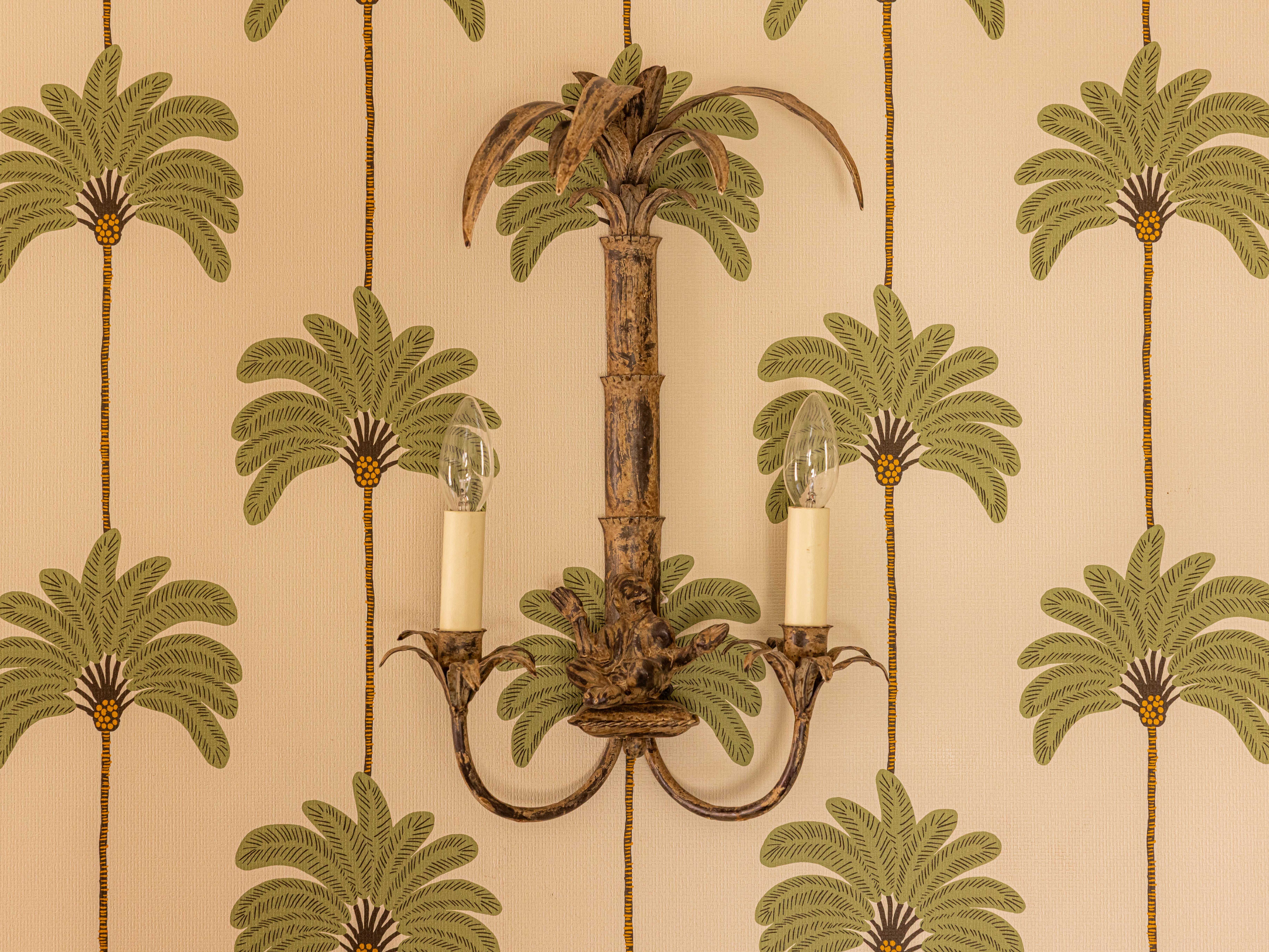 Victorian style wall light fixture mounted on a wall with tropical palm tree pattern wallpaper