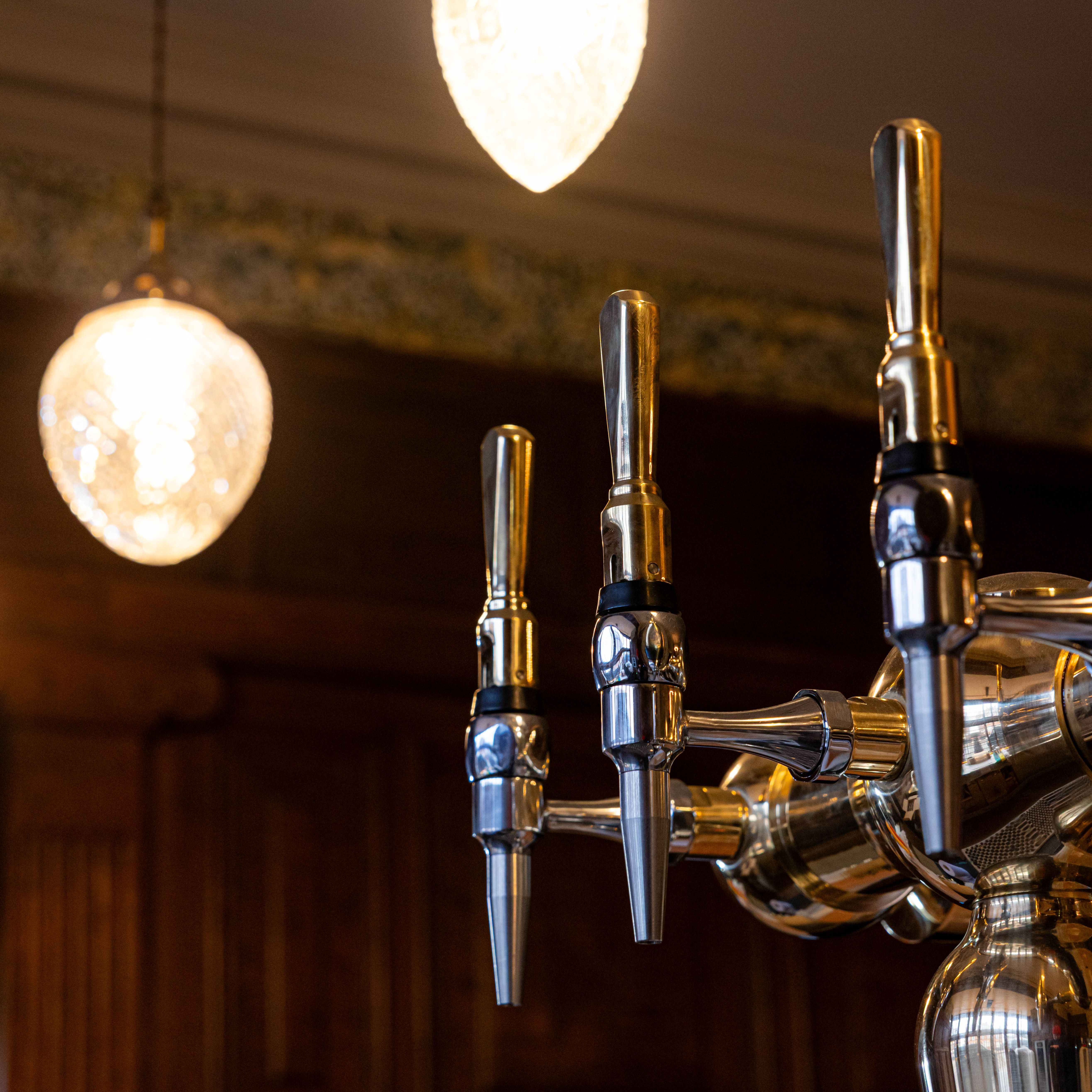 Close-up of shiny bar taps with ornate ceiling lights above
