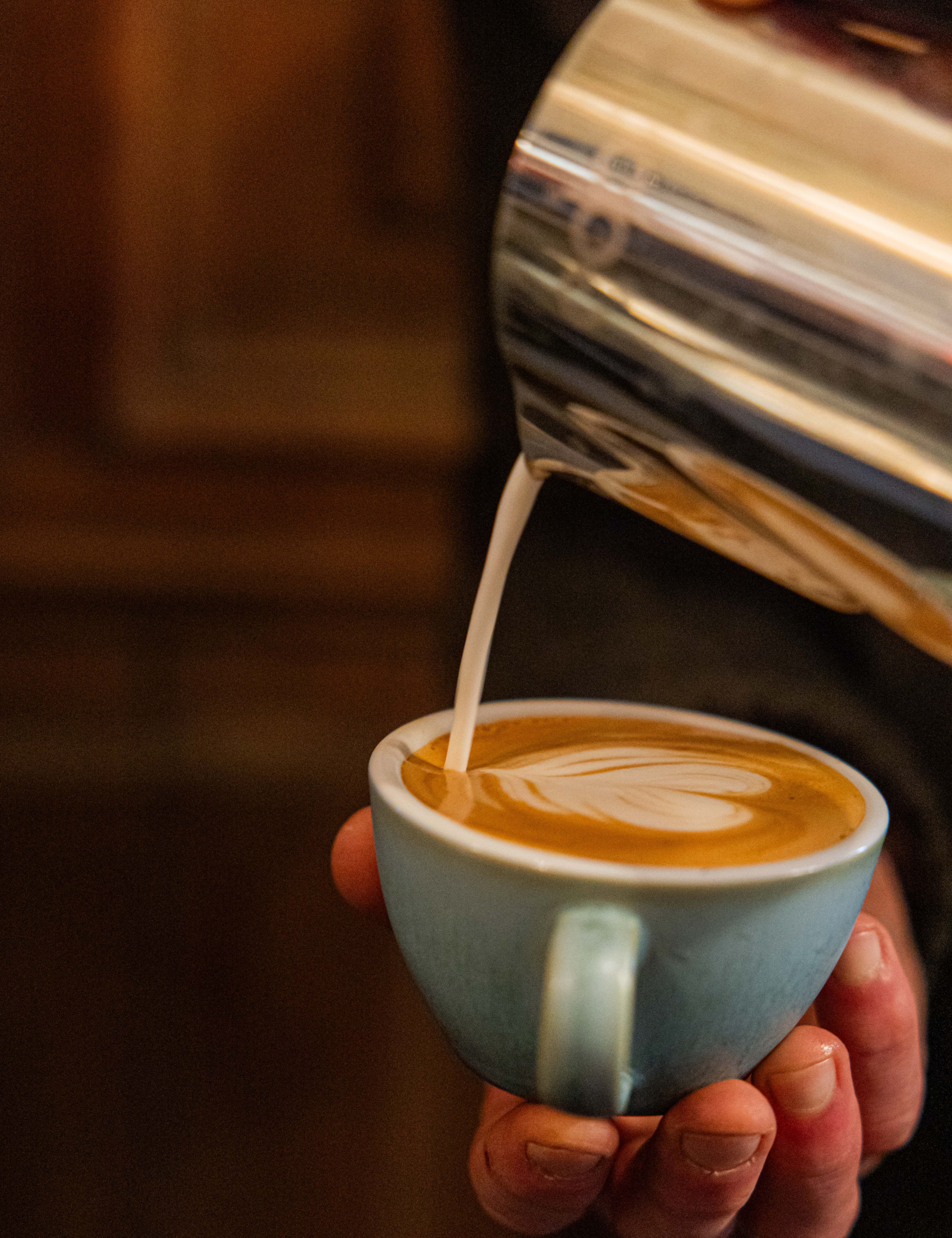 Barista pouring steamed milk into a cup of coffee to create latte art