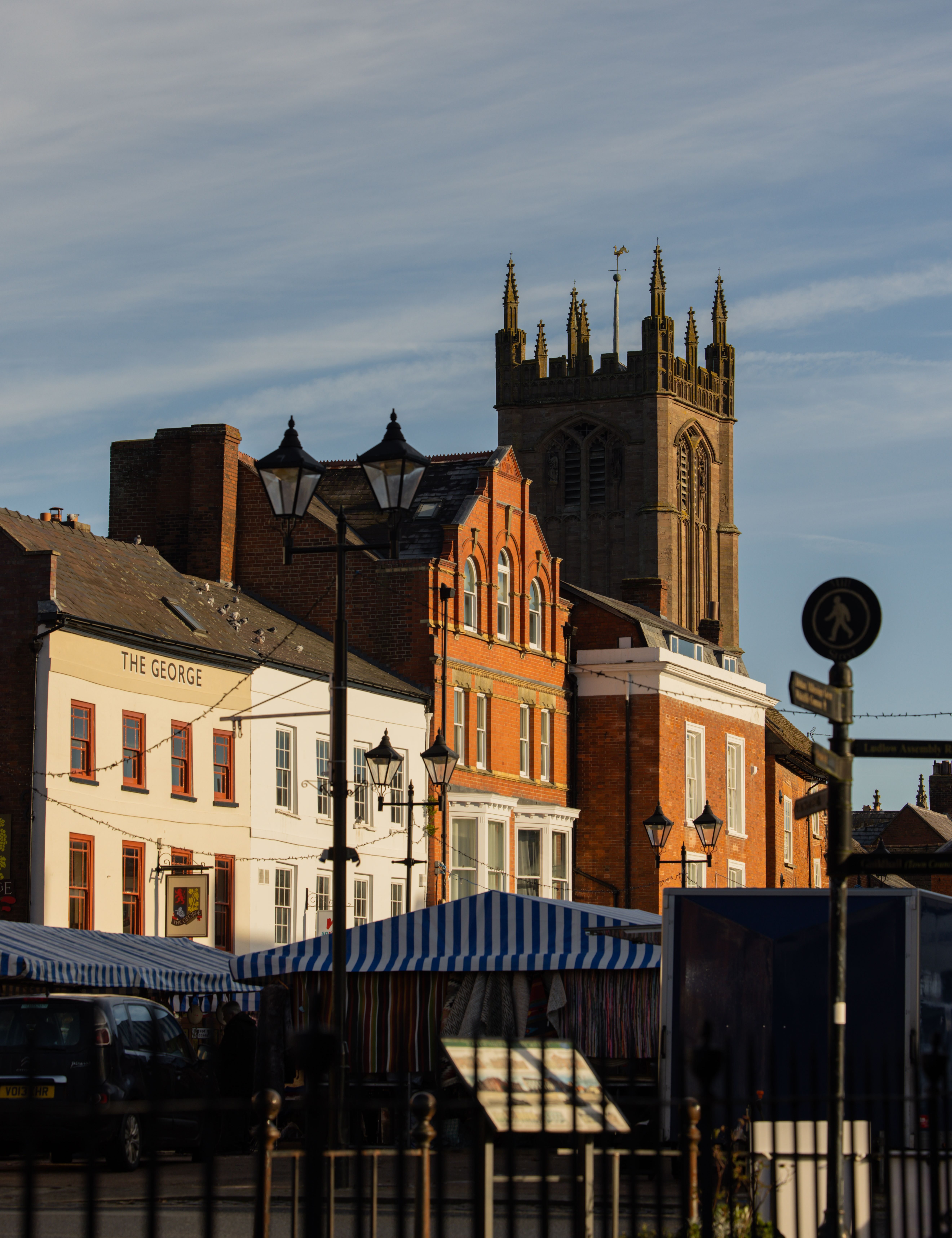 Market square with striped market stalls, historic buildings, and a church tower in the background under a blue sky.