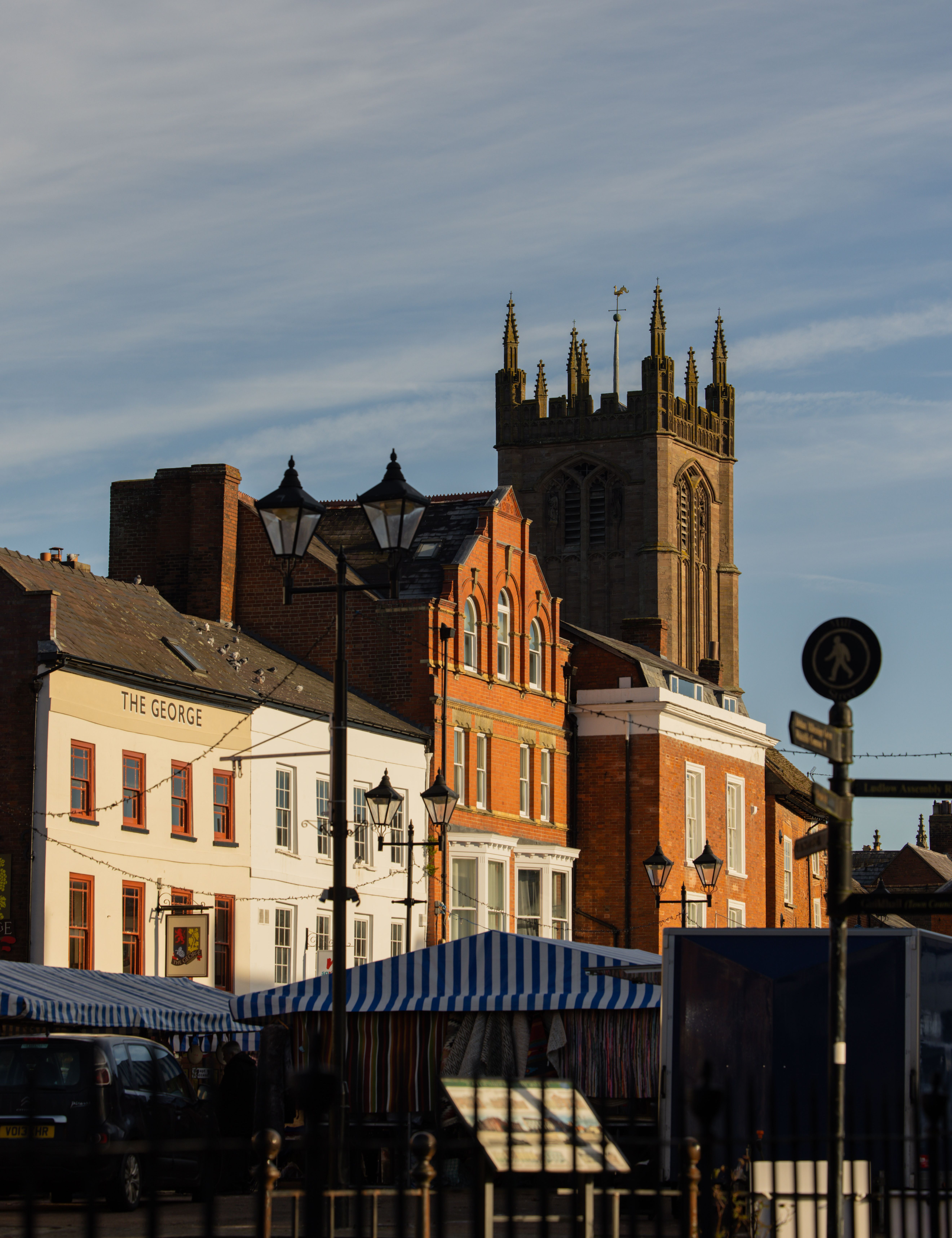 Market square with striped market stalls, historic buildings, and a church tower in the background under a blue sky.