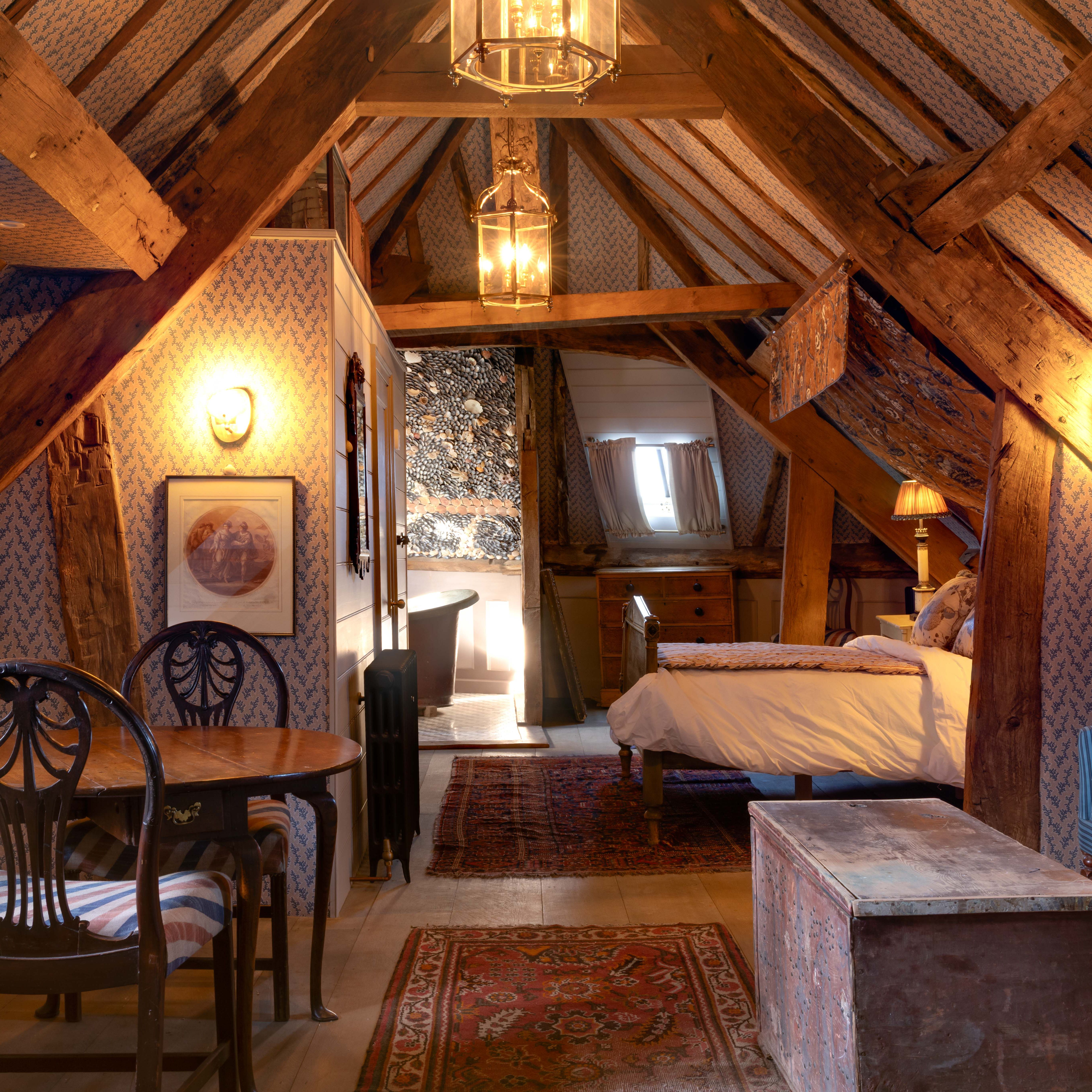 Cozy attic suite with rustic wooden beams, vintage furniture, and a small dining and kitchen area.