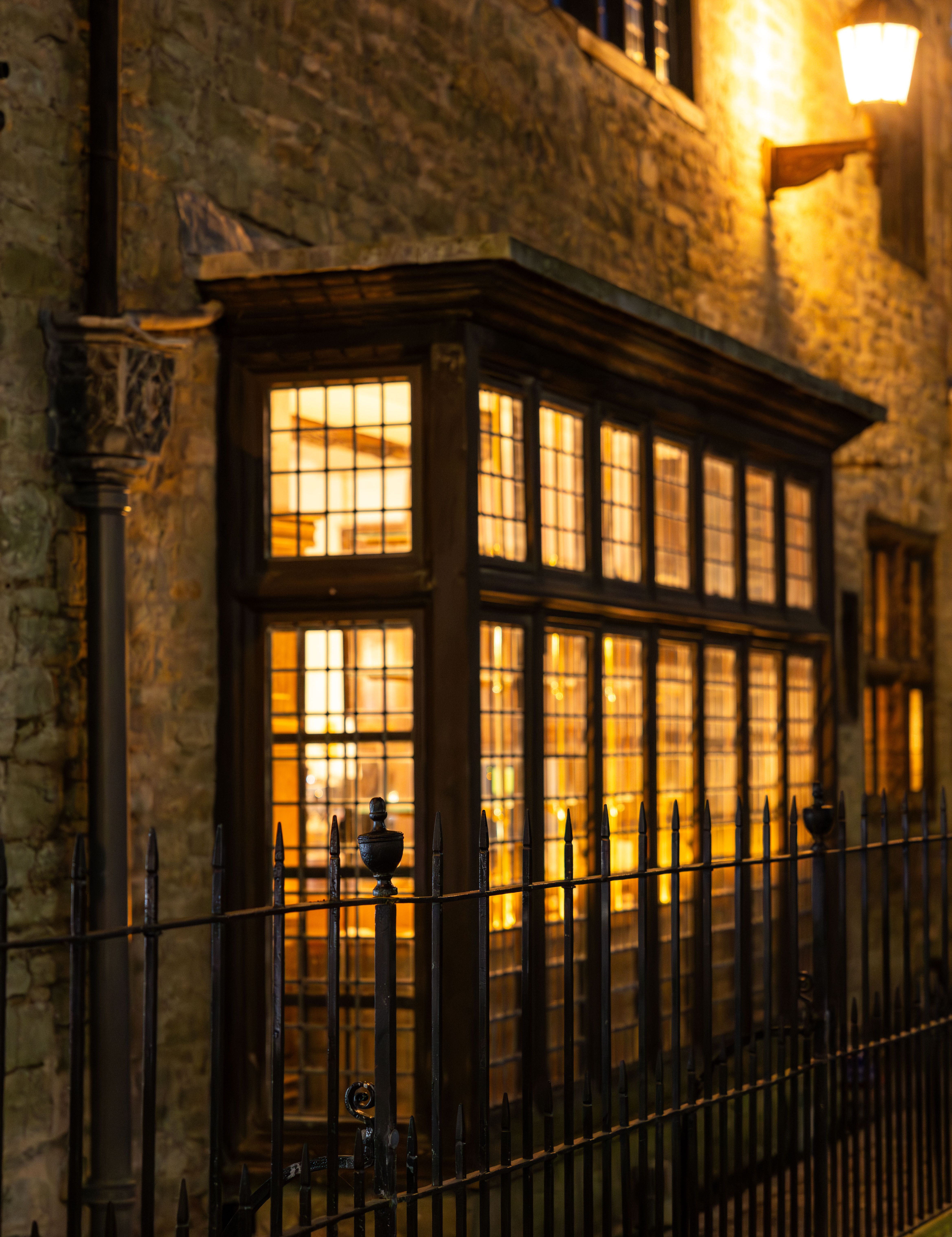 Warmly lit bar exterior at night with large windows and wrought iron fence