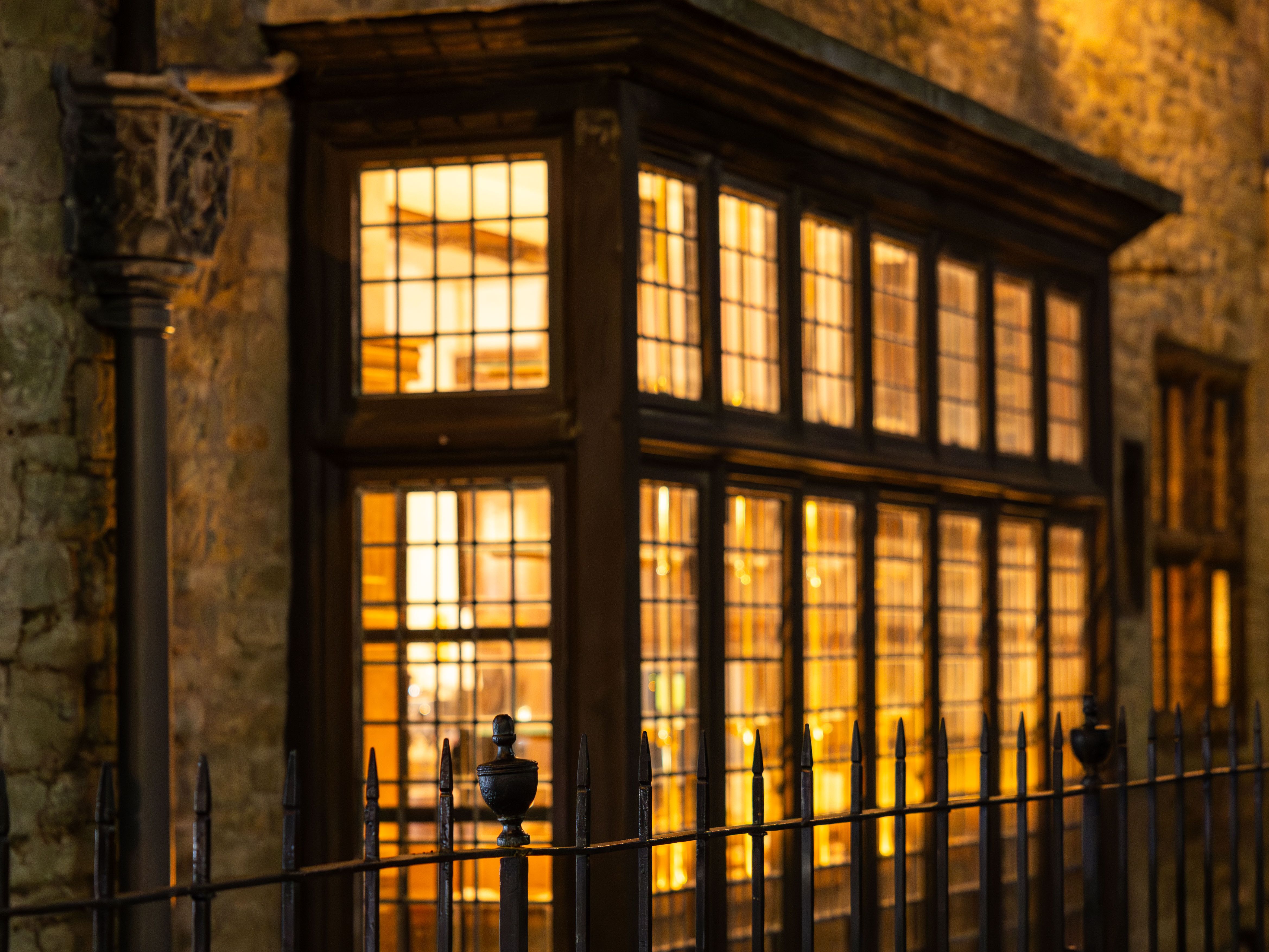Warmly lit bar exterior at night with large windows and wrought iron fence