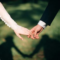 Close-up of bride and groom holding hands outdoors, casting a heart-shaped shadow