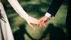Close-up of bride and groom holding hands outdoors, casting a heart-shaped shadow
