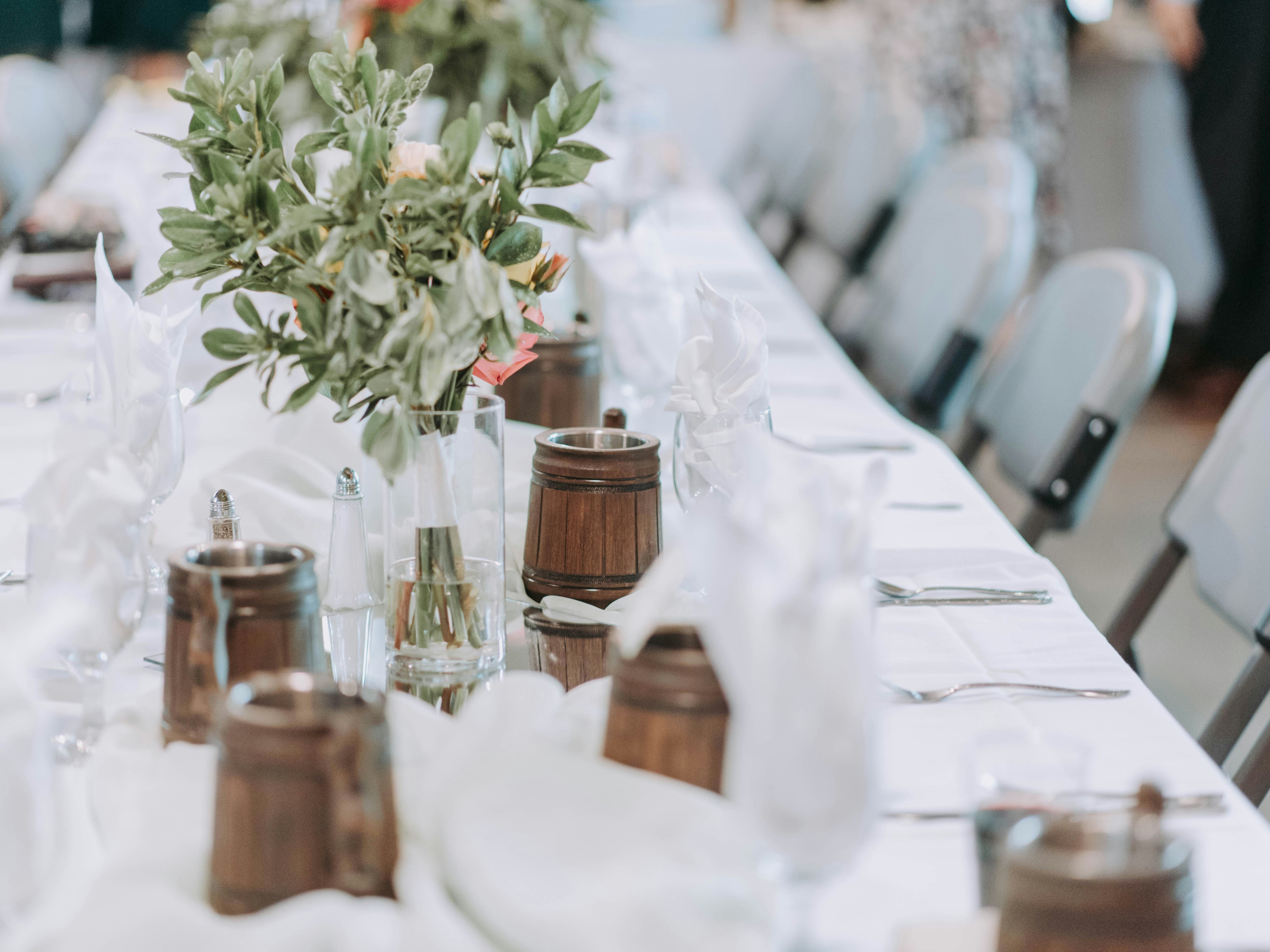 Elegant table setting with floral centerpieces and wooden mugs at a formal event.