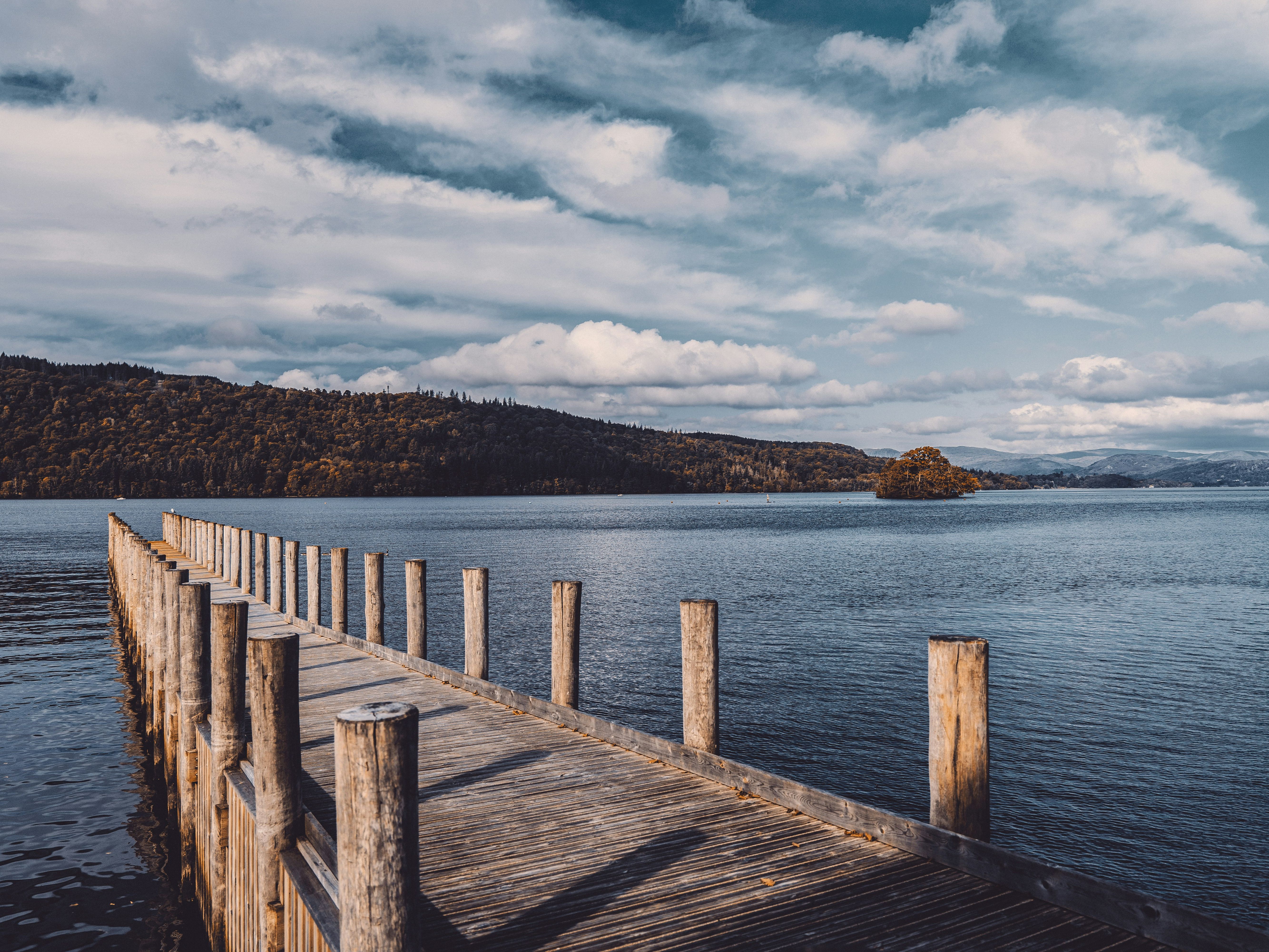 Wooden pier extending into a calm lake with hills and trees in the background under a cloudy sky