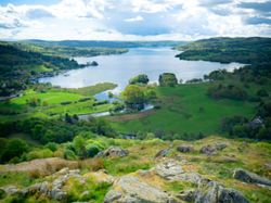 A scenic landscape view of a lake surrounded by green hills and rocky terrain under a dramatic cloudy sky.