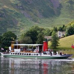 A passenger boat cruising on a lake with green hills and a house in the background.
