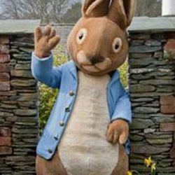 A person in a Peter Rabbit costume waving in front of a brick and stone wall.
