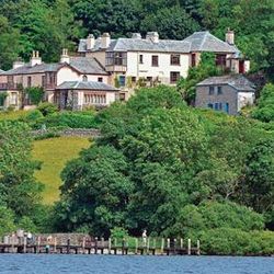 Large houses surrounded by trees on a hillside overlooking a lake with a wooden dock in the foreground.