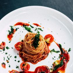 Plated spaghetti pasta with tomato sauce, cherry tomatoes, and herbs on a white dish
