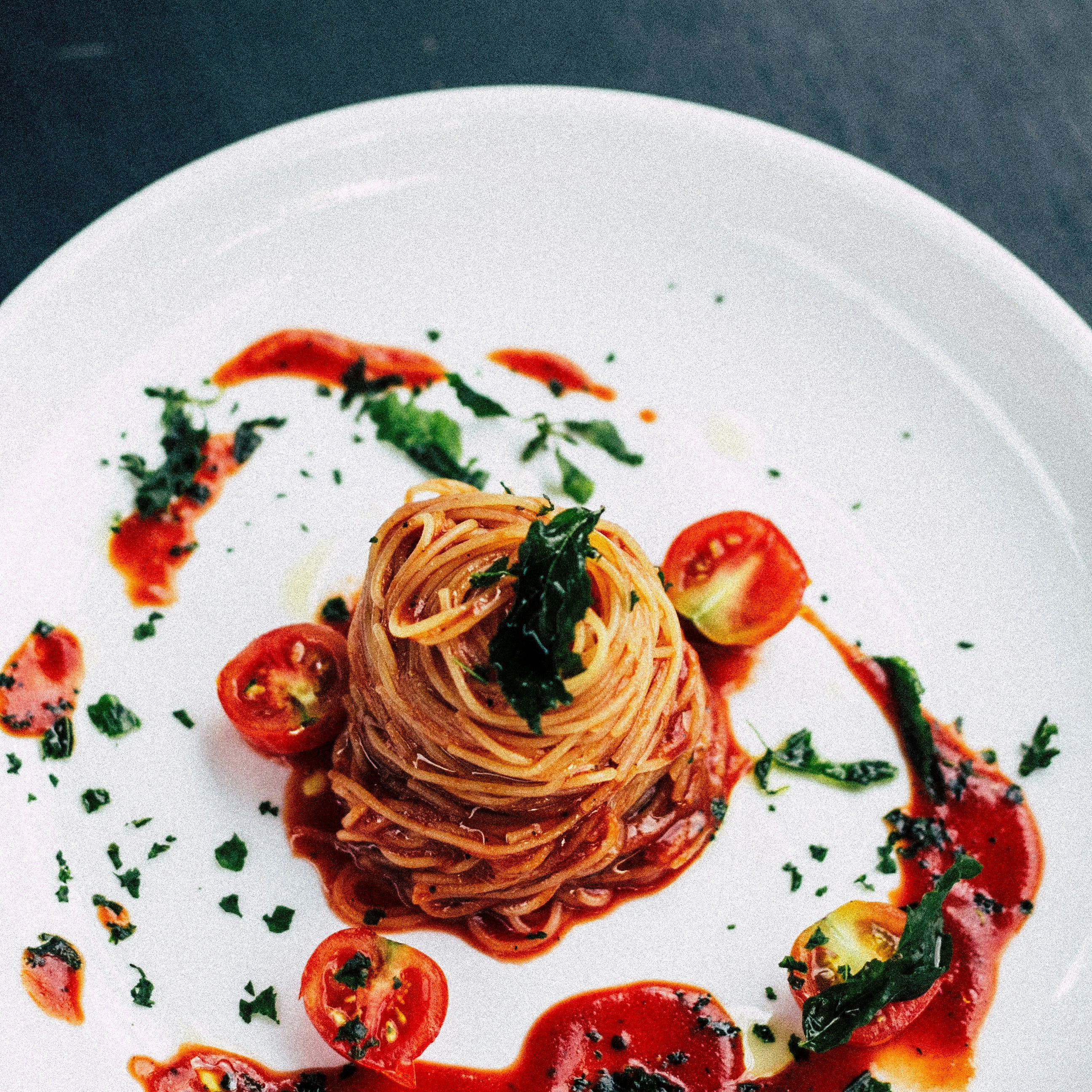 Plated spaghetti pasta with tomato sauce, cherry tomatoes, and herbs on a white dish