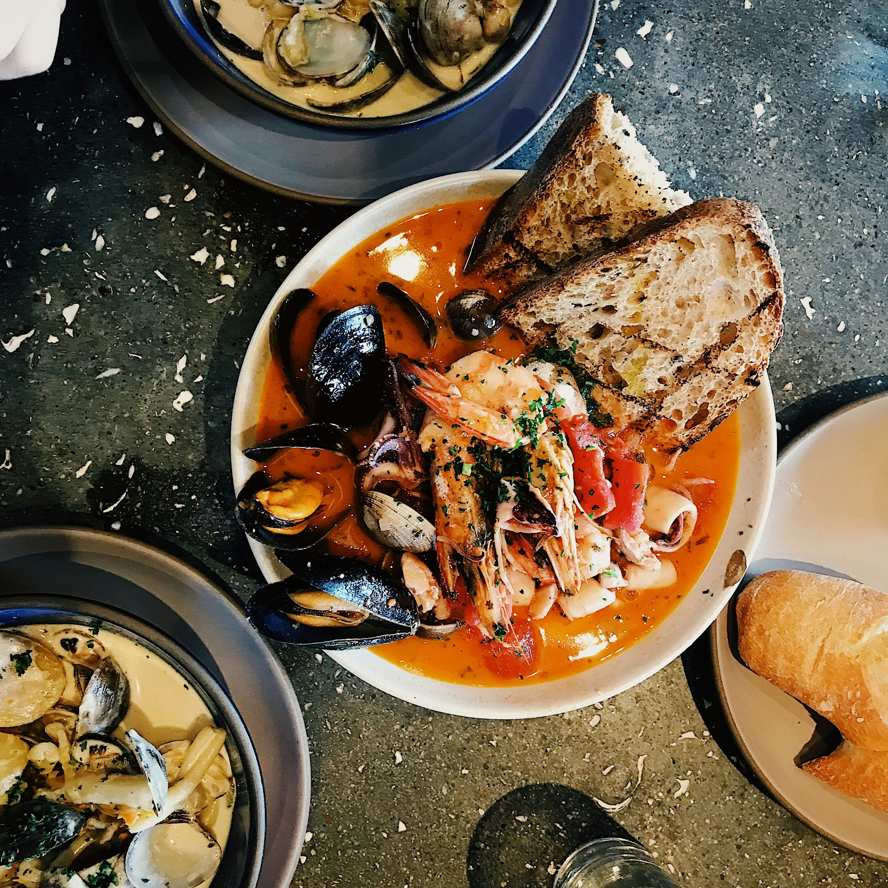 Overhead view of seafood dishes including mussels, shrimp, clams, toasted bread, and creamy pasta