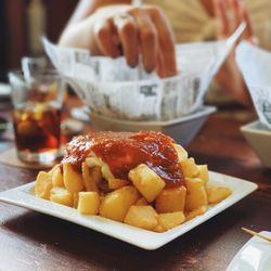 Plate of patatas bravas, Spanish fried potatoes topped with spicy tomato sauce and mayonnaise, on a wooden table with a person in the background